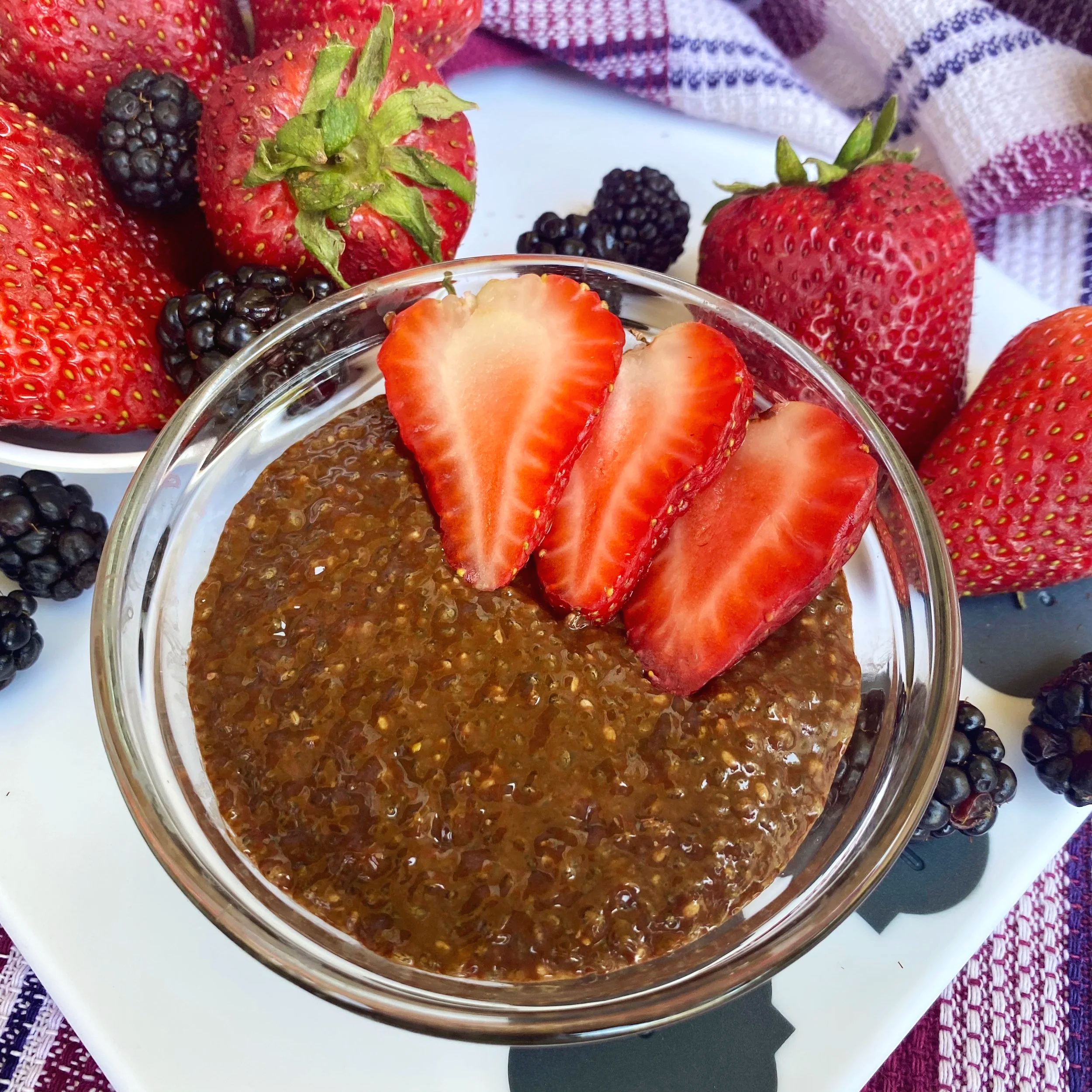 Fresh strawberries and blackberries surrounding a bowl of chia seed pudding topped with sliced strawberries.