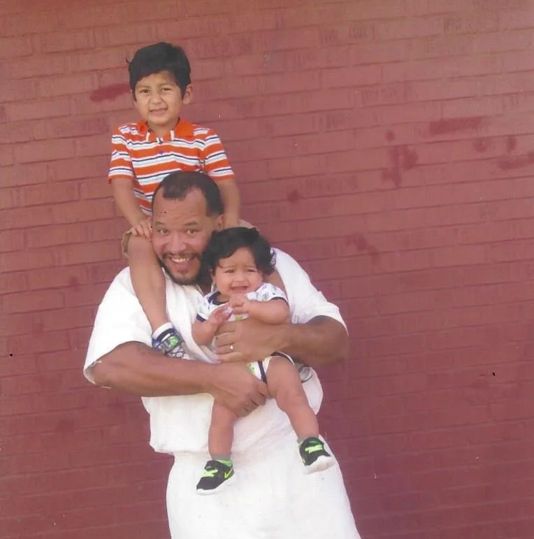 Nanon Williams holding his niece and nephew on his shoulders against a red brick wall.
