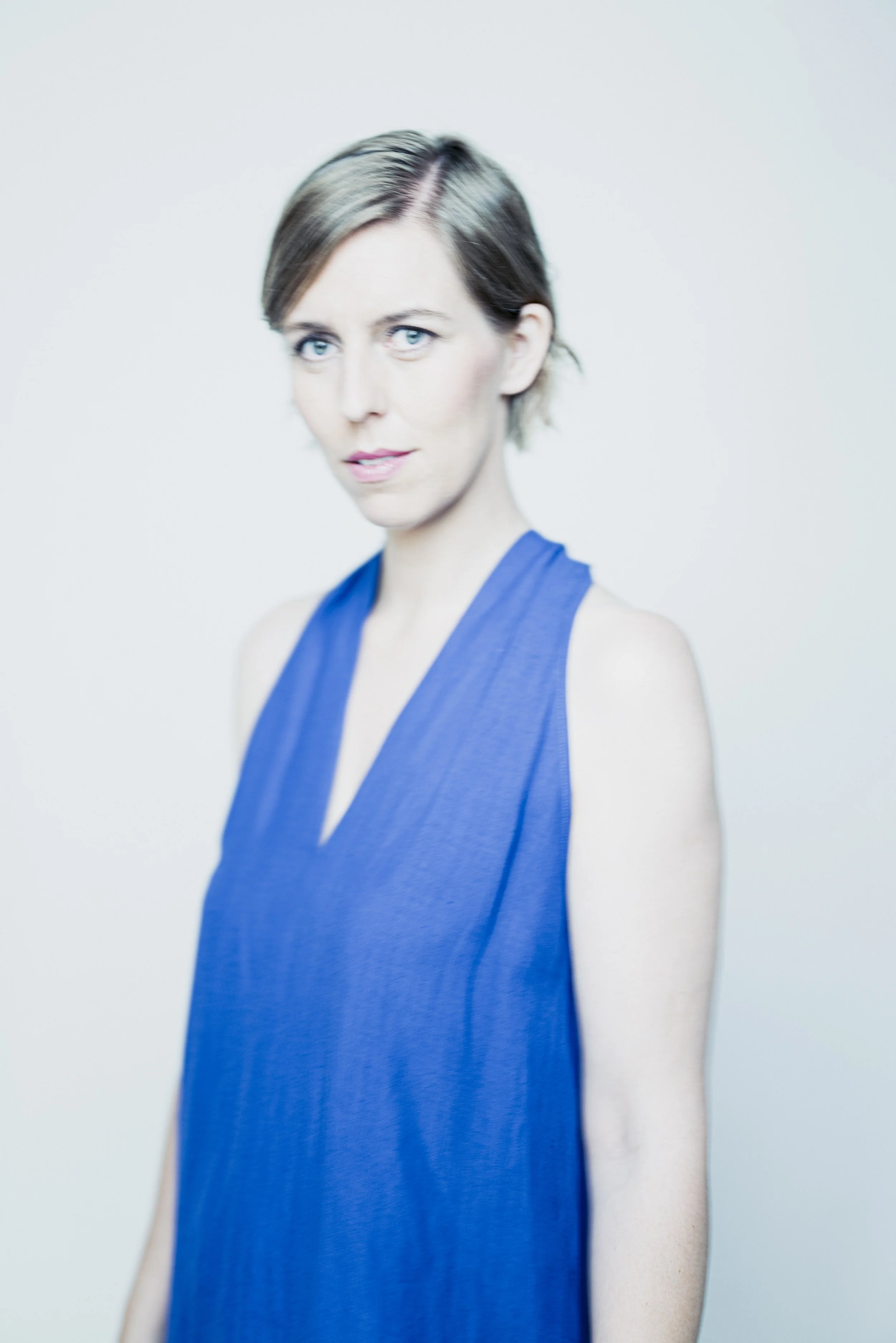 Porträt einer Frau mit kurzen braunen Haaren, blauen Augen und blauer ärmelloser Bluse vor hellem Hintergrund.