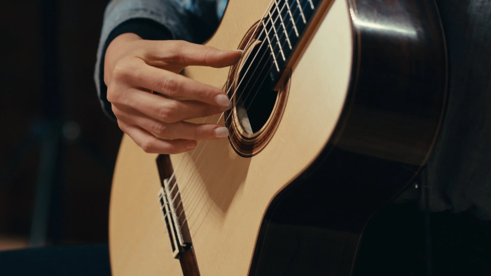 Nahaufnahme einer Person, die auf einer Akustikgitarre spielt, fokussiert auf die Hand, die die Saiten berührt.