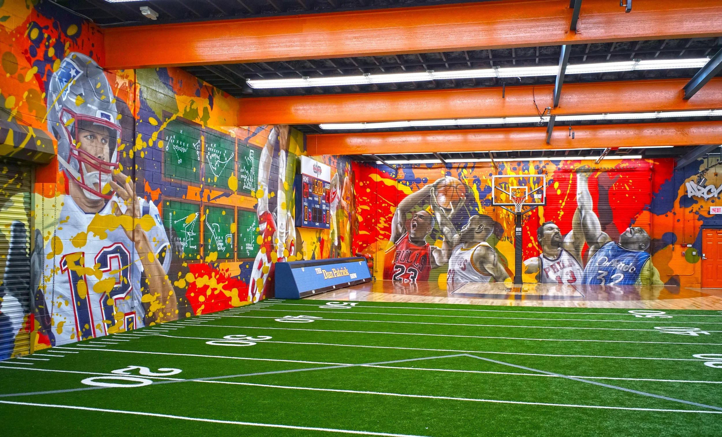 Indoor sports facility featuring vibrant wall murals of famous basketball players with graffiti-style painted background, a small artificial turf football field with yard lines, and a basketball hoop. THE DAN PATRICK SHOW MILFORD CONNECTICUT ARCY