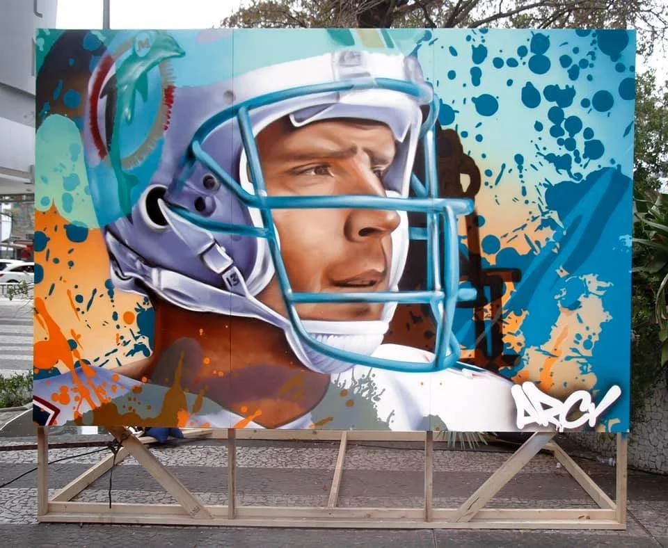 Colorful street art mural depicting a football player wearing a helmet, with abstract splashes of blue, orange, and beige in the background. DAN MARINO ARCY LIVE EVENT MURALS THE DAN PATRICK SHOW MIAMI FLORIDA SUPER BOWL WEEK