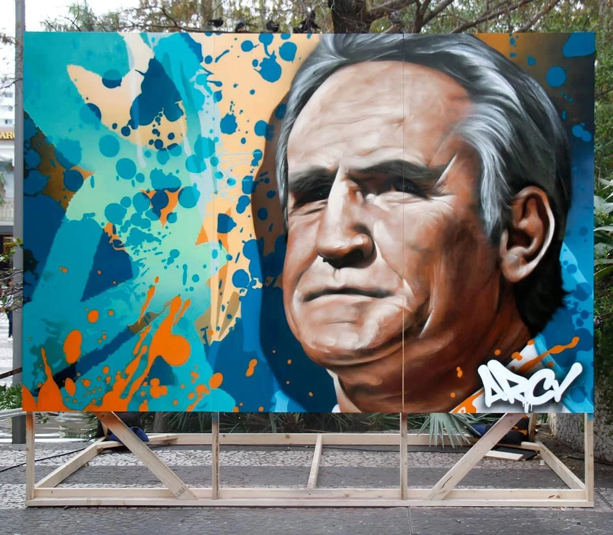 Graffiti-style mural of a serious-looking elderly man with gray hair, painted on a large, colorful canvas with blue, orange, and beige splashes DON SHULA ARCY LIVE EVENT MURALS THE DAN PATRICK SHOW MIAMI FLORIDA SUPER BOWL WEEK