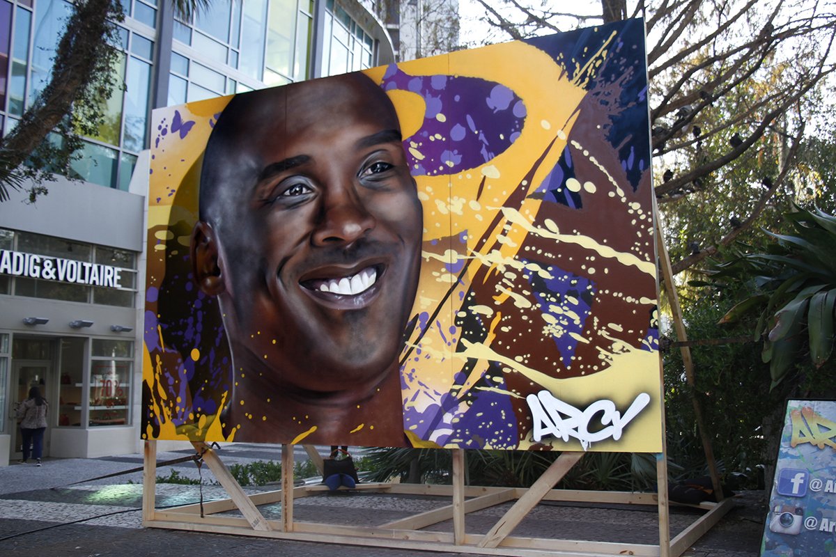 Large graffiti-style mural of a smiling man with dark skin and a shaved head, with abstract splashes KOBE BRYANT THE LOST ANGELES LAKERS MIAMI FLORIDA THE DAN PATRICK SHOW SUPER BOWL WEEK