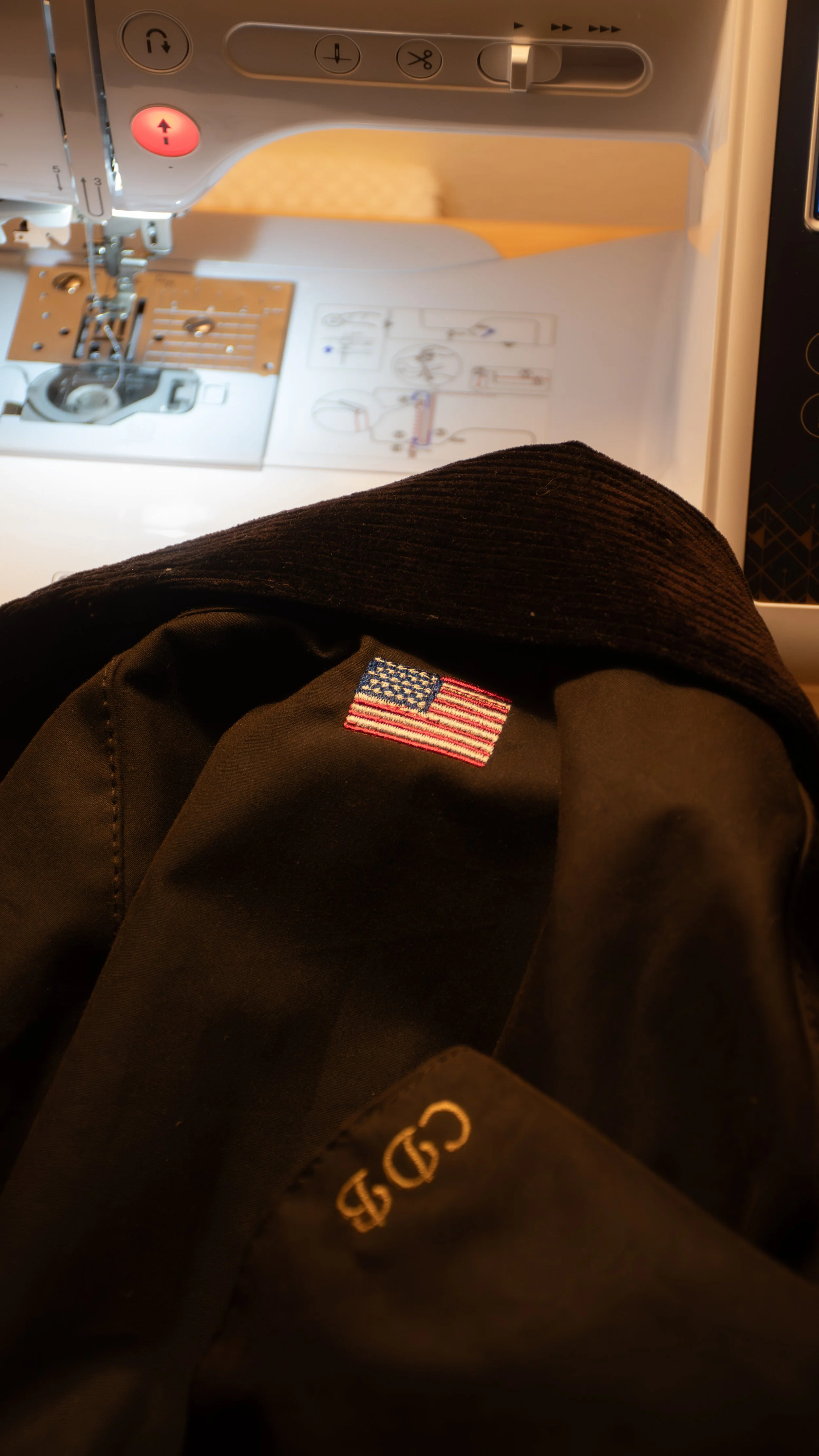 Close-up view of a sewing machine with instructions and buttons visible, and a person's knee and American flag patch on their clothing in the foreground.