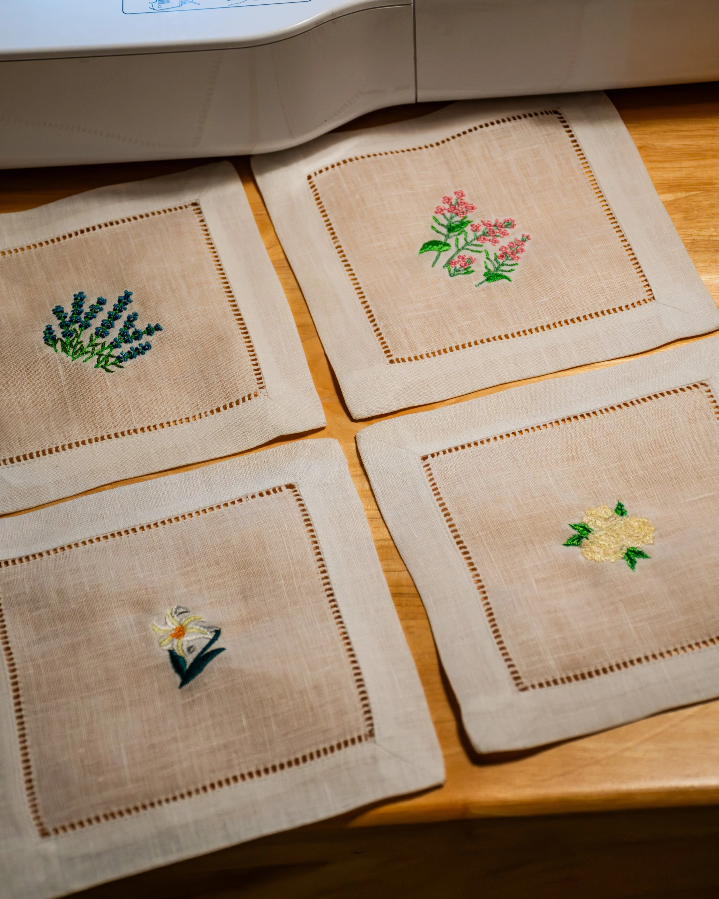 Close-up view of several embroidered cross-stitch cloth pieces with floral and nature designs on a wooden surface.