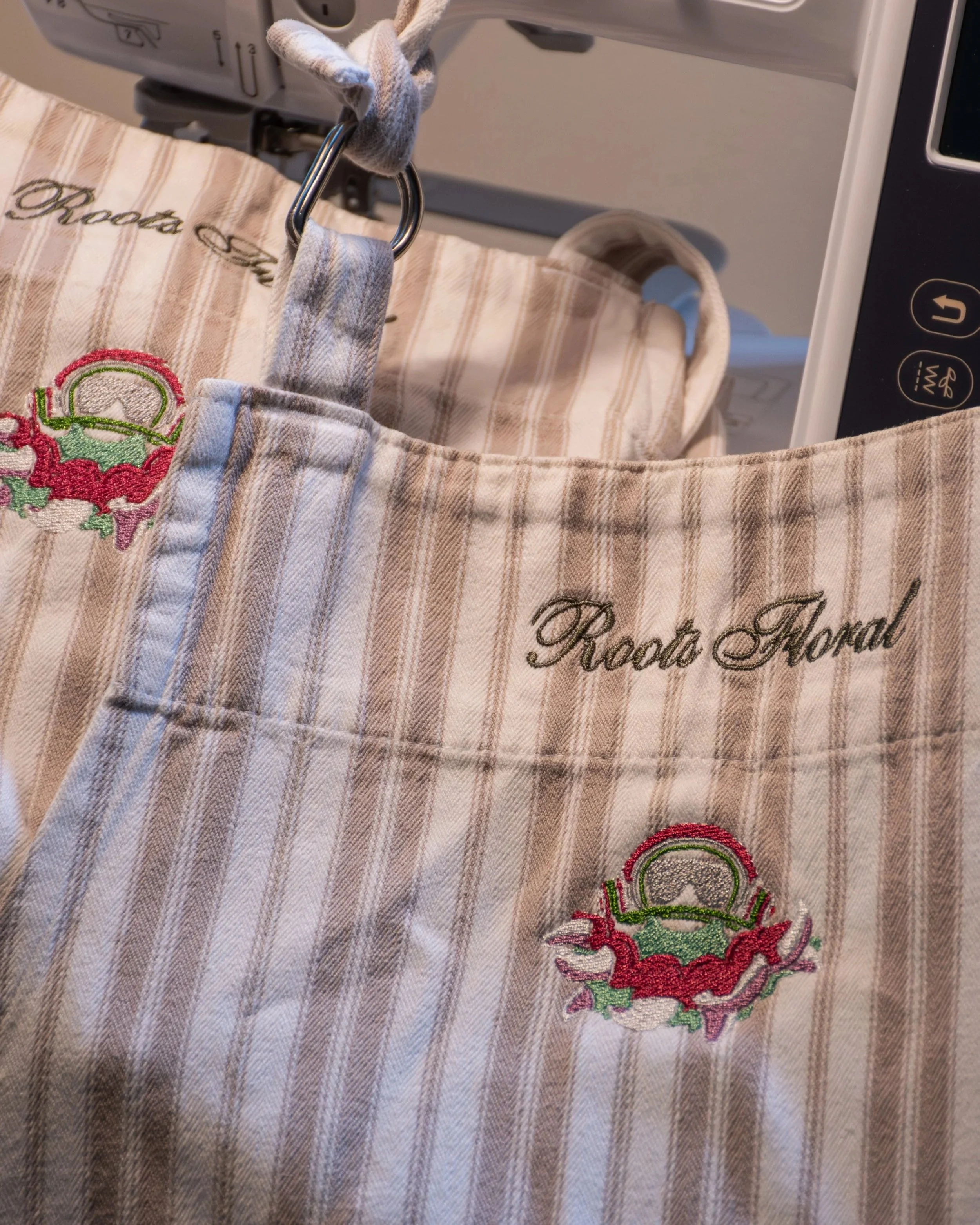 Close-up of embroidery on beige and white plaid fabric, featuring a red and green floral design and black cursive text.