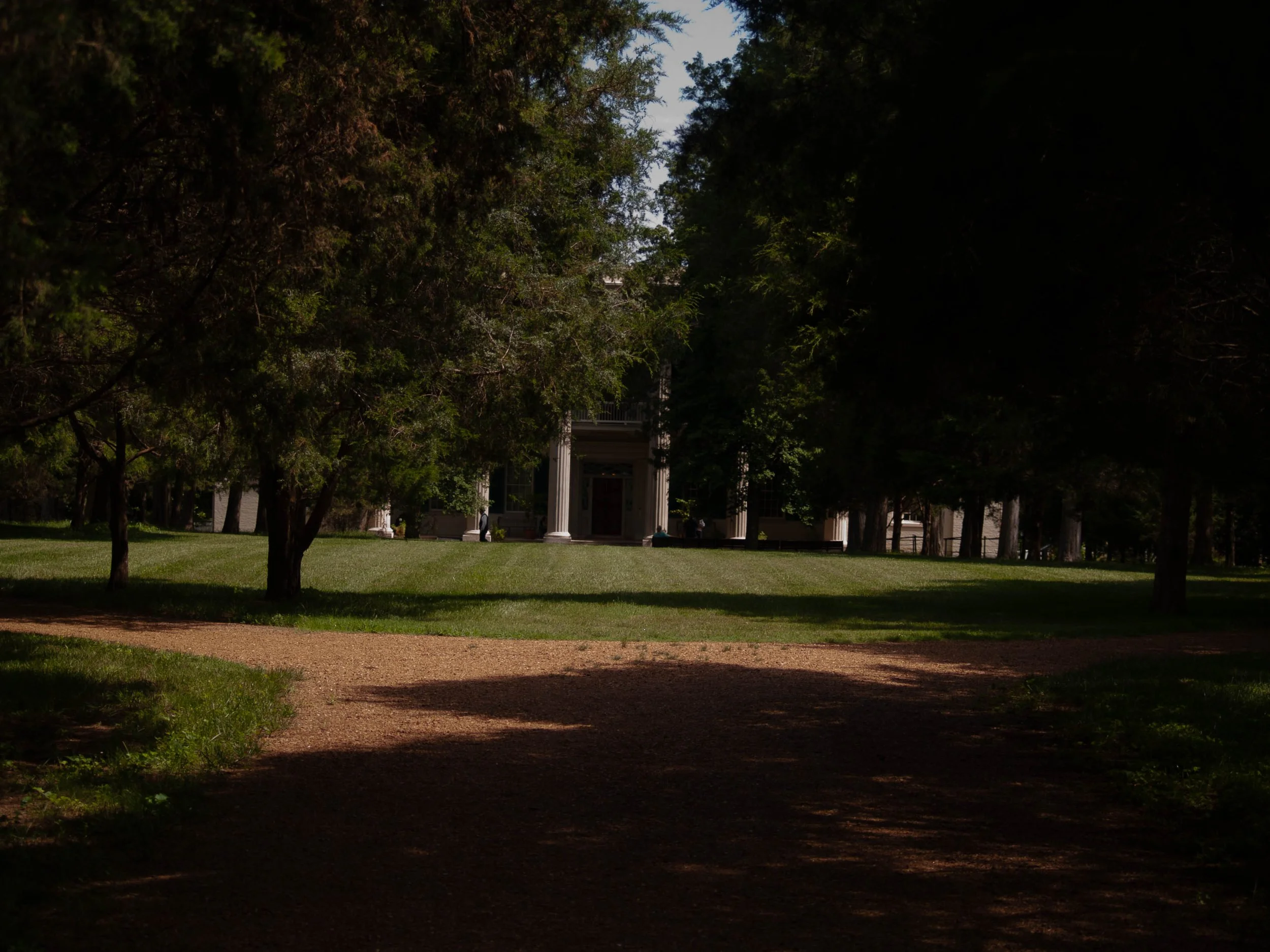 A large building with columns is visible through trees in a park or garden.