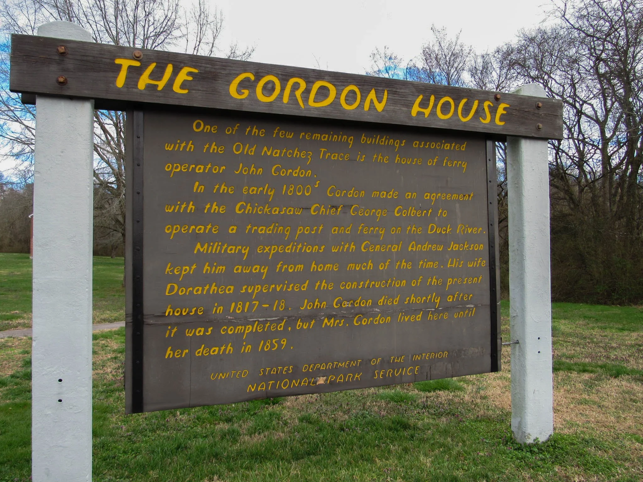 Historical sign about The Gordon House at Chickasaw National Recreation Area, describing its history and construction, with trees and grass in the background.