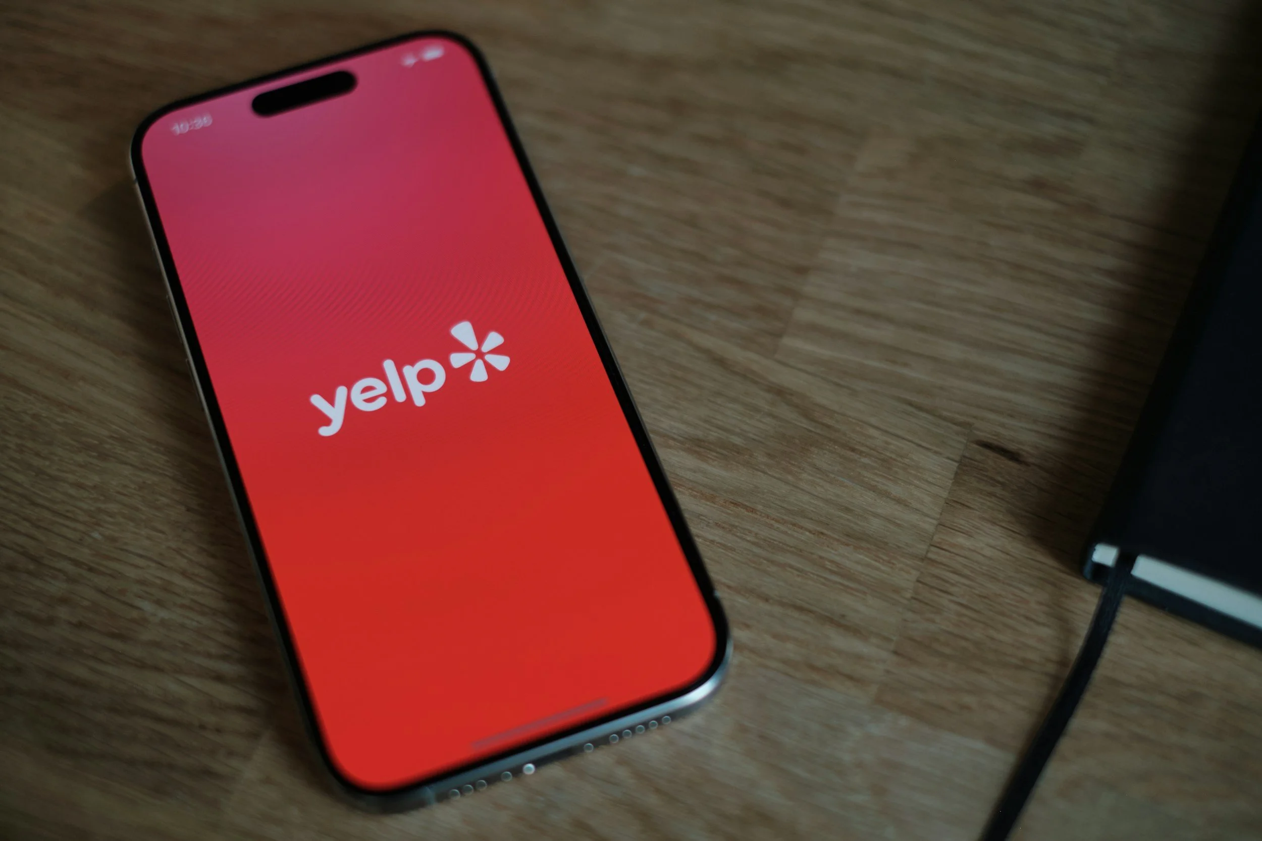 Smartphone on wooden surface displaying the Yelp app logo on the screen.