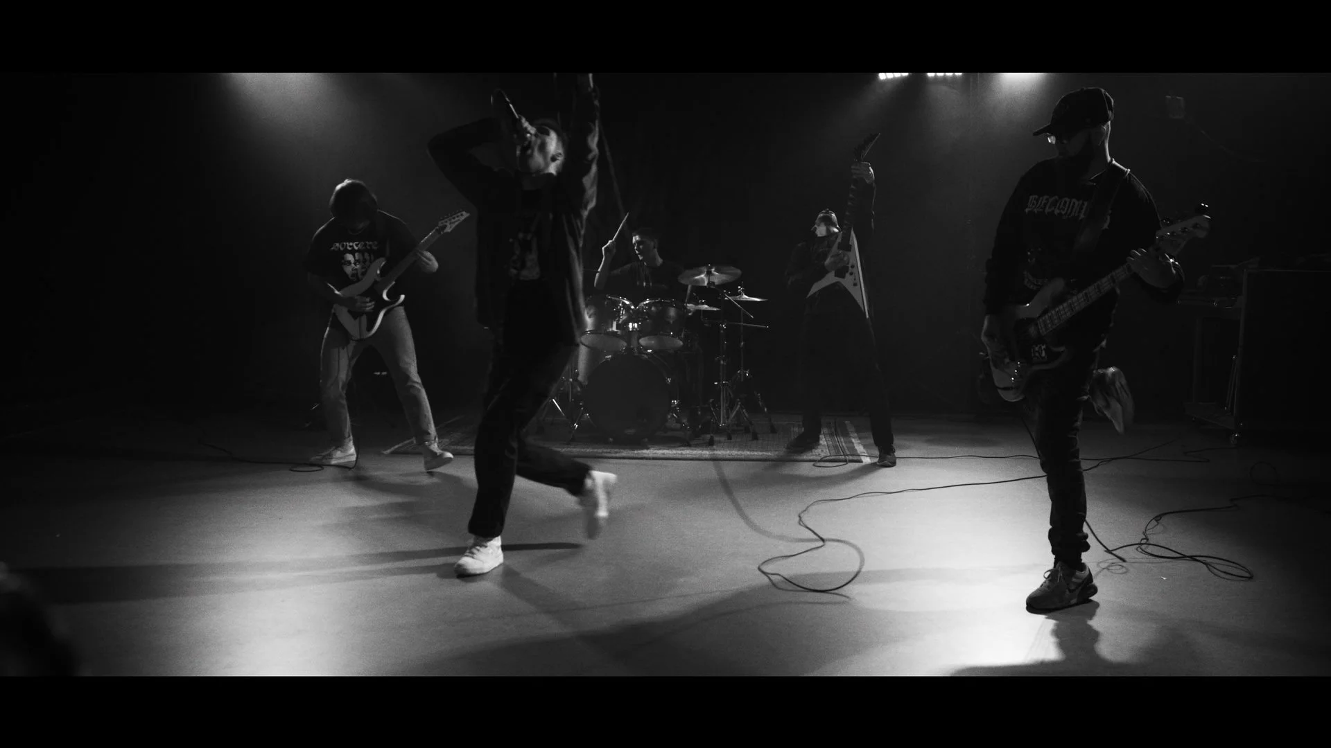 Eine Gruppe junger Musiker spielt auf einer dunklen Bühne, begleitet von instrumenten wie Gitarre, Schlagzeug und Bass, bei einer Live-Performance.