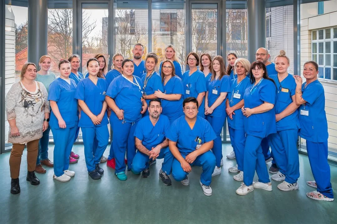 Gruppenfoto von Krankenhauspersonal in blauen OP-Kräften in einem hellen Raum mit großen Fenstern und Blick auf städtische Gebäude im Hintergrund.