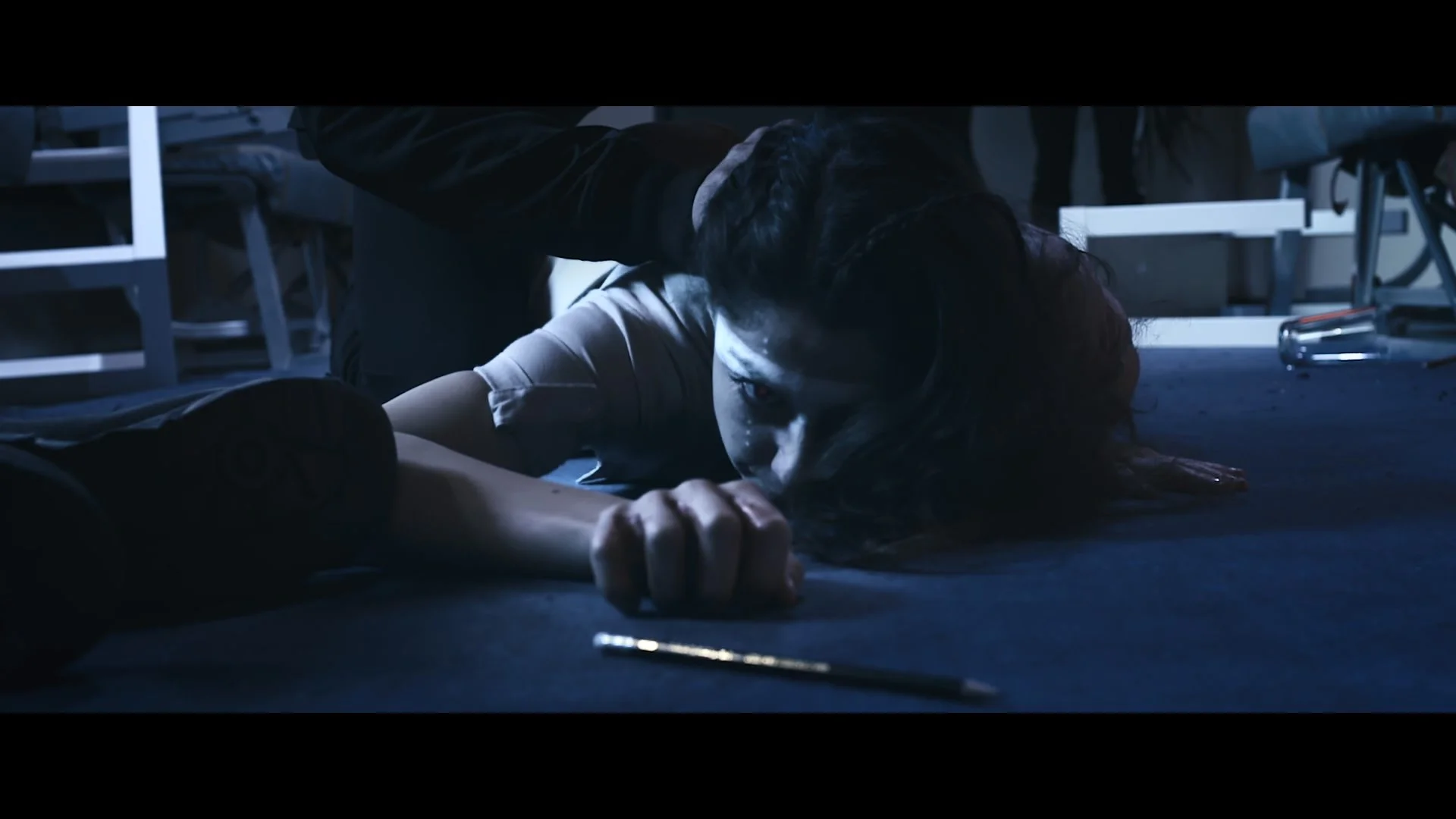 Eine Frau liegt blutüberströmt am Boden und sieht erschöpft oder traumatisiert aus, während eine Hand sie berührt.