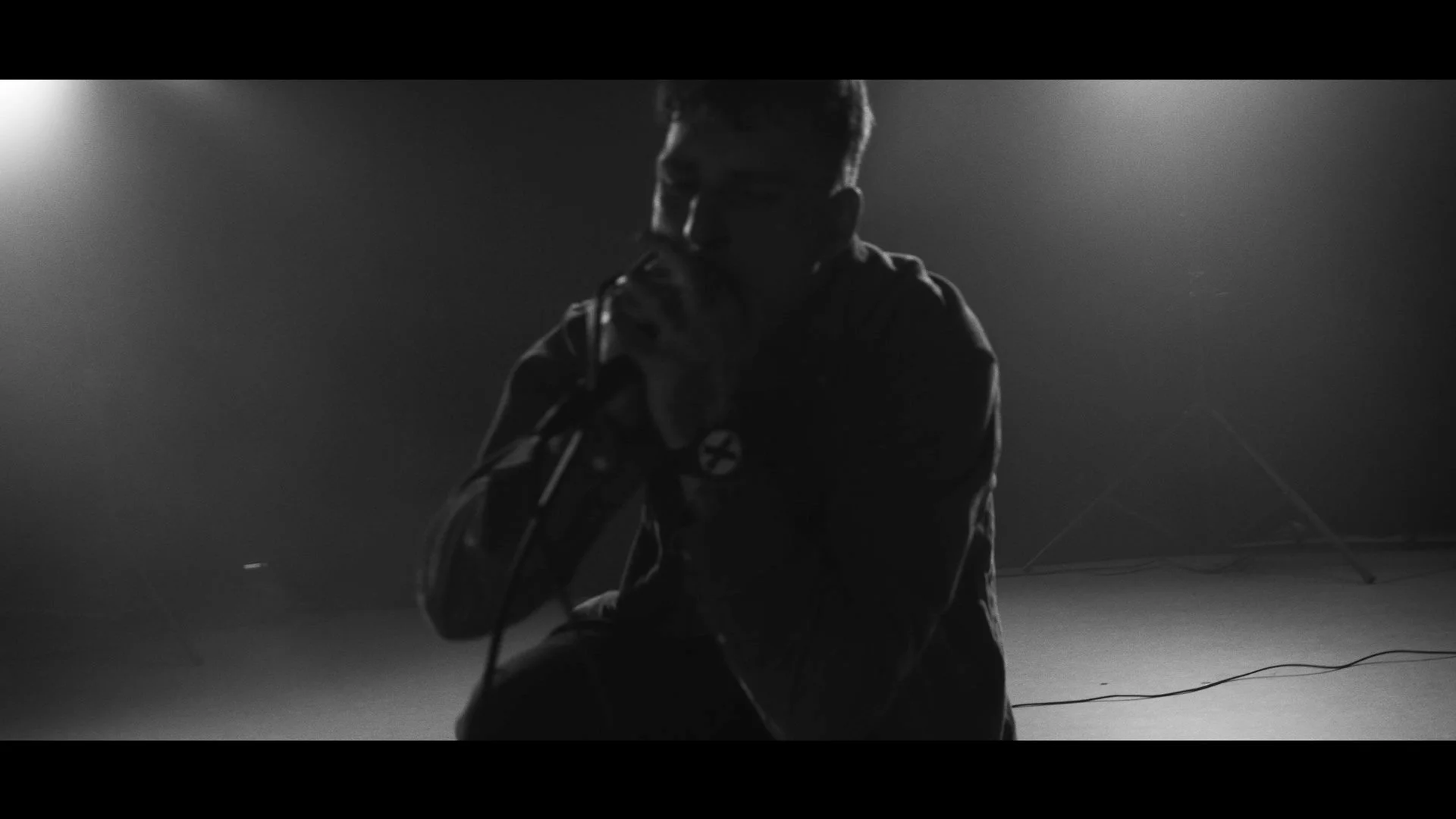 Schwarzes und weißes Bild eines Mannes, der in die Kamera singt, während er einen Mikrofon hält, in einem dunklen Raum mit gerichteter Beleuchtung