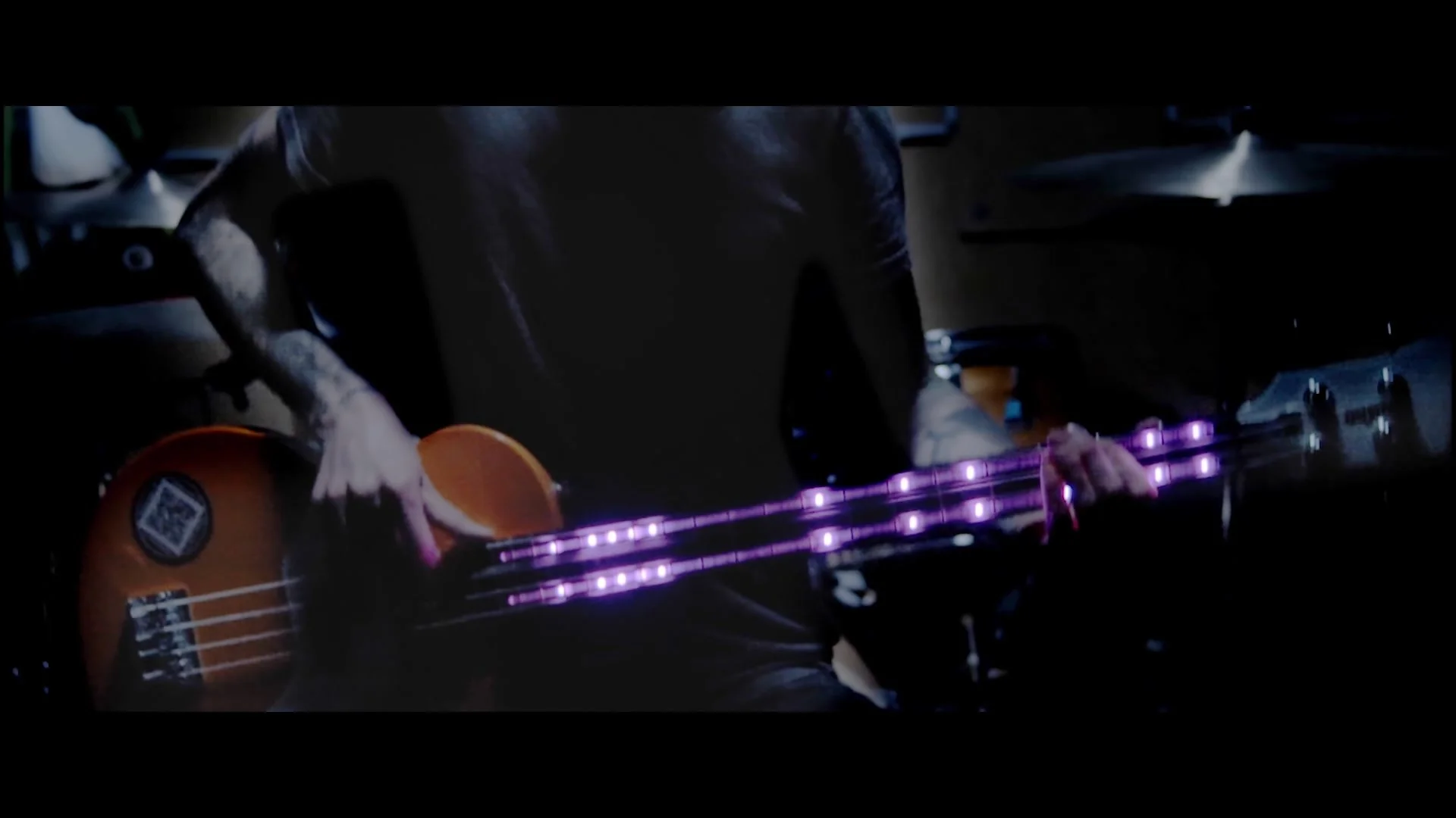 Person spielt Bassgitarre mit leuchtenden Saiten in einem dunklen Raum.