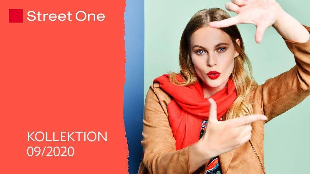 Eine Frau trägt eine braune Jacke und einen roten Schal, macht eine Handgeste und schaut in die Kamera.