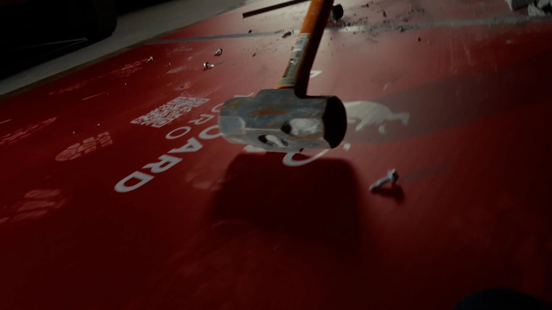 A hammer is resting on a red surface with white text and a logo, with small debris scattered nearby.