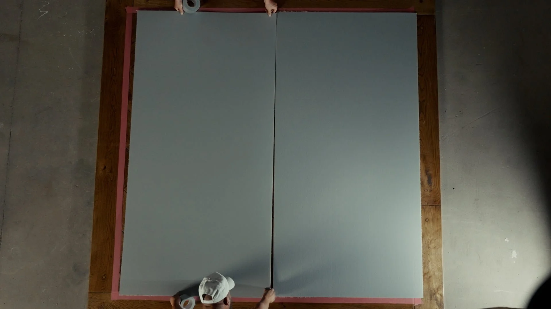 Overhead view of two people preparing a gray ping pong table with pink border on a concrete floor.