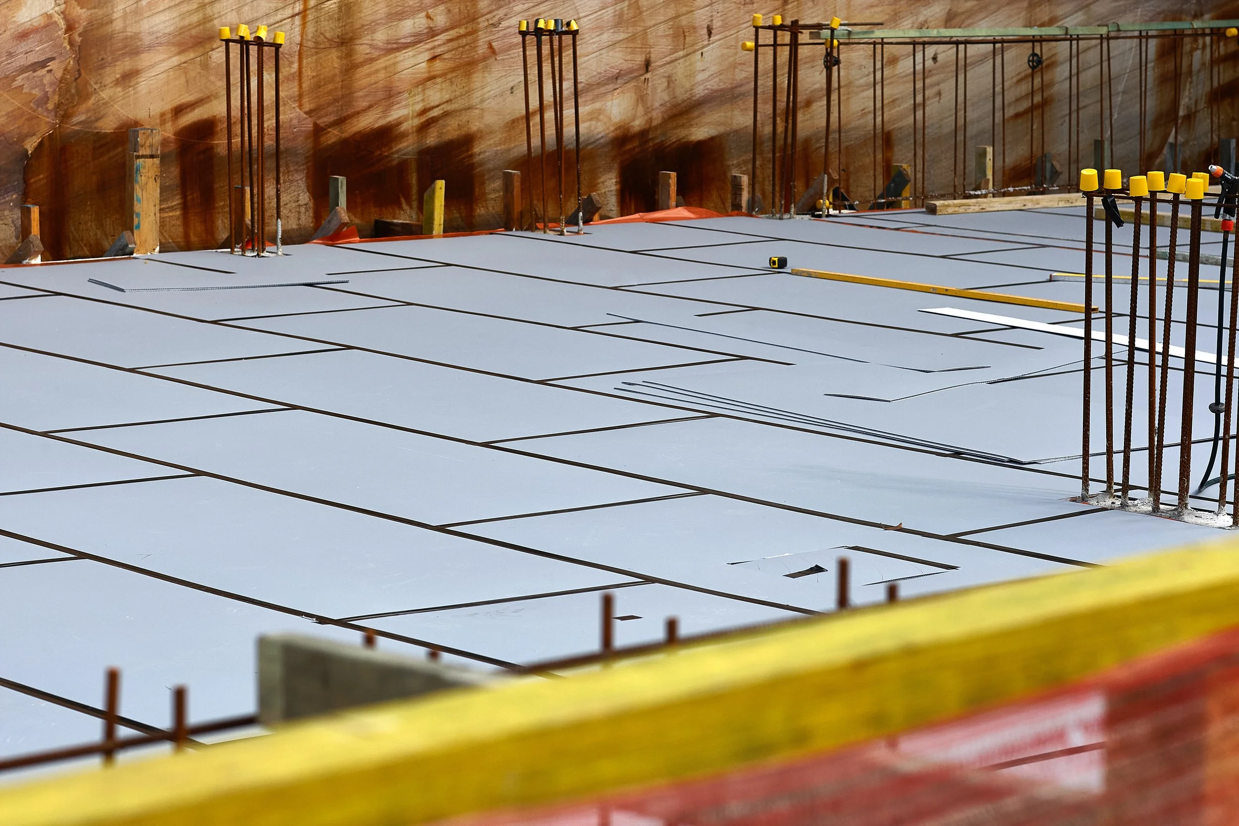 Construction site with rebar and concrete foundation, wooden formwork, and orange safety barriers.