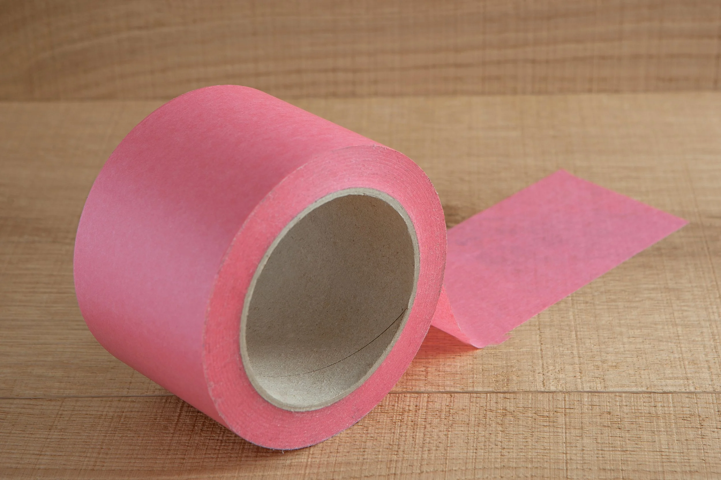 A roll of pink sports tape unrolled on a wooden surface.
