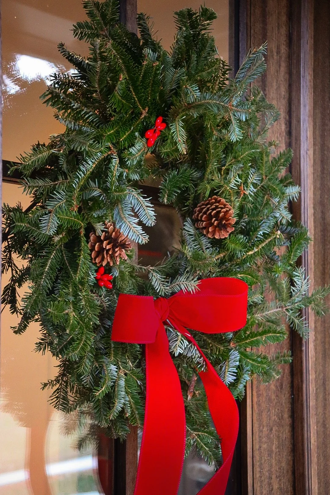 Little Porch Decorators Christmas wreath with pinecones and red berries on wooden door