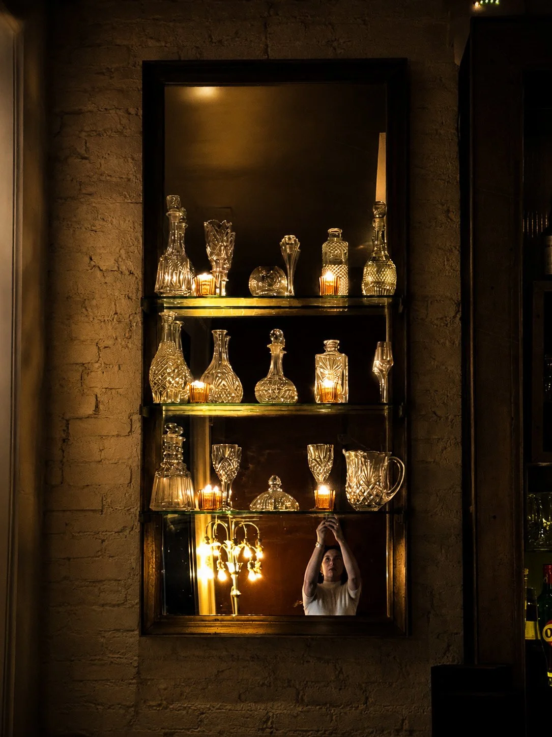 Bar mirror reflection with glass decanters, candles, and chandelier, New York