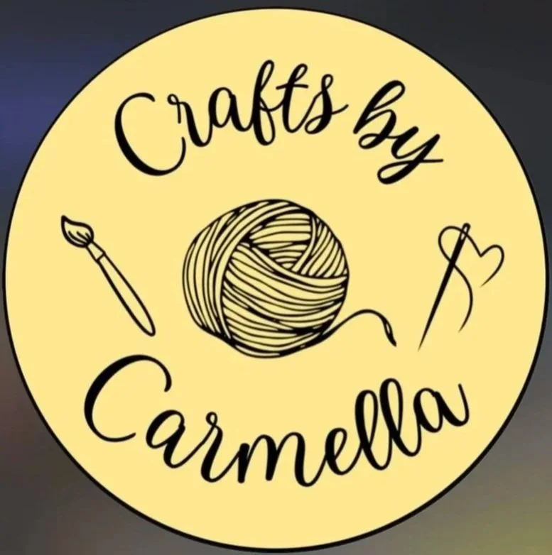 Yellow circle logo for Crafts by Carmella. A ball of yarn, a paint brush, and a needle with thread are centered in the circle with an outer black boarder