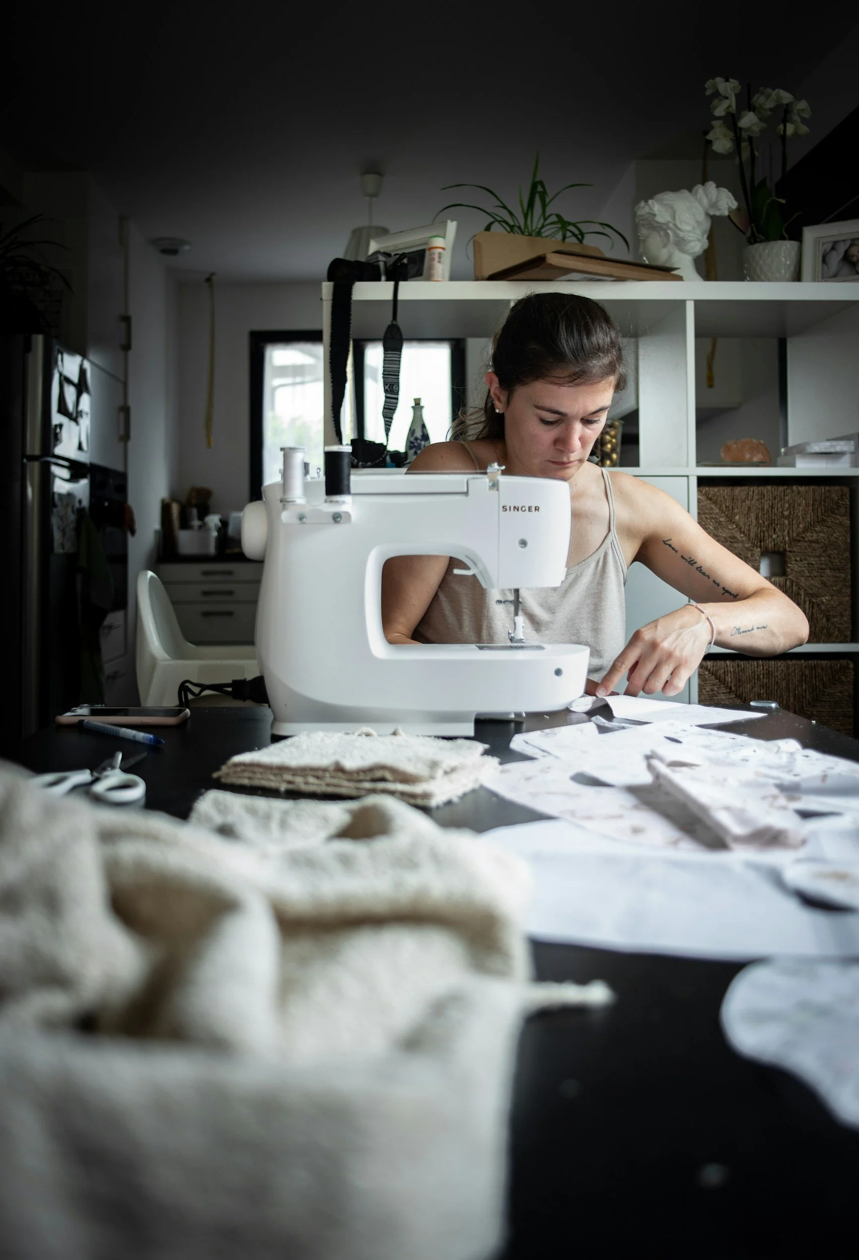 woman at sewing machine working on a project with patterns and fabric all over the table