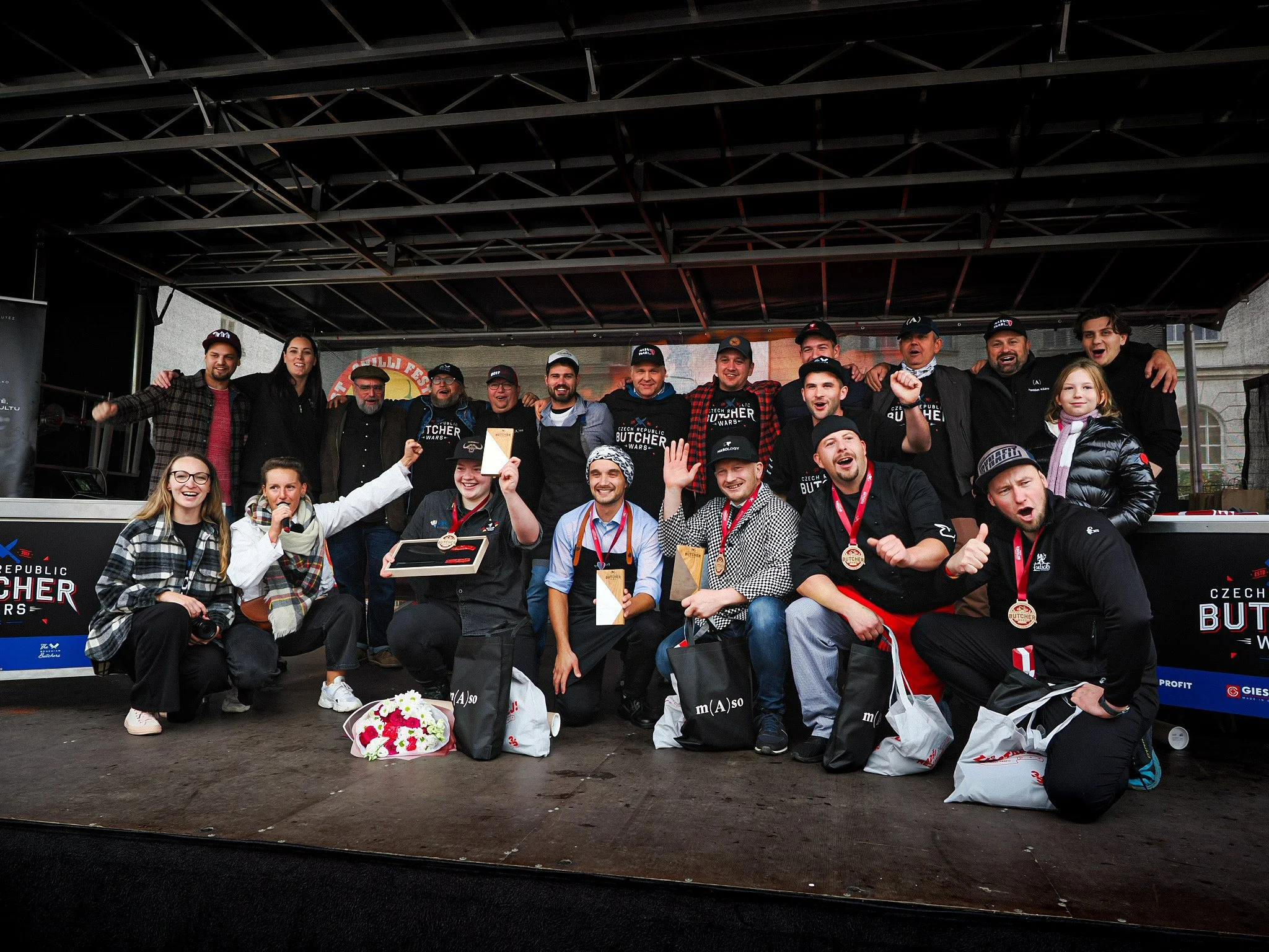 Group of people celebrating on stage at a culinary competition event, some holding awards and medals, smiling and posing for a photo.