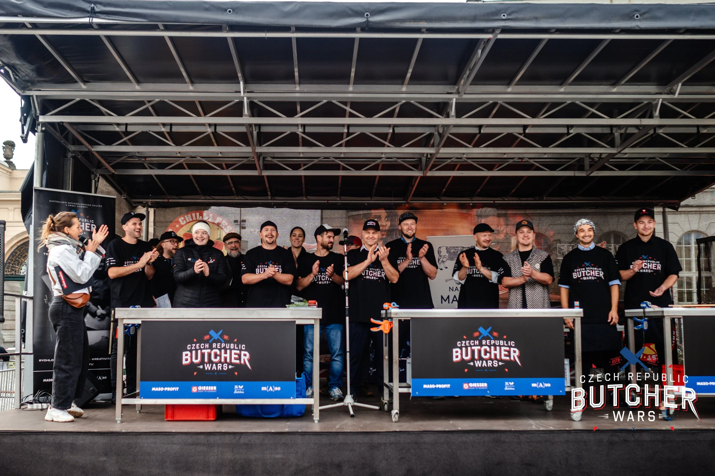 Group of people on stage at the Czech Republic Butcher Wars event, clapping and smiling, with banners and screens displaying event branding behind them.
