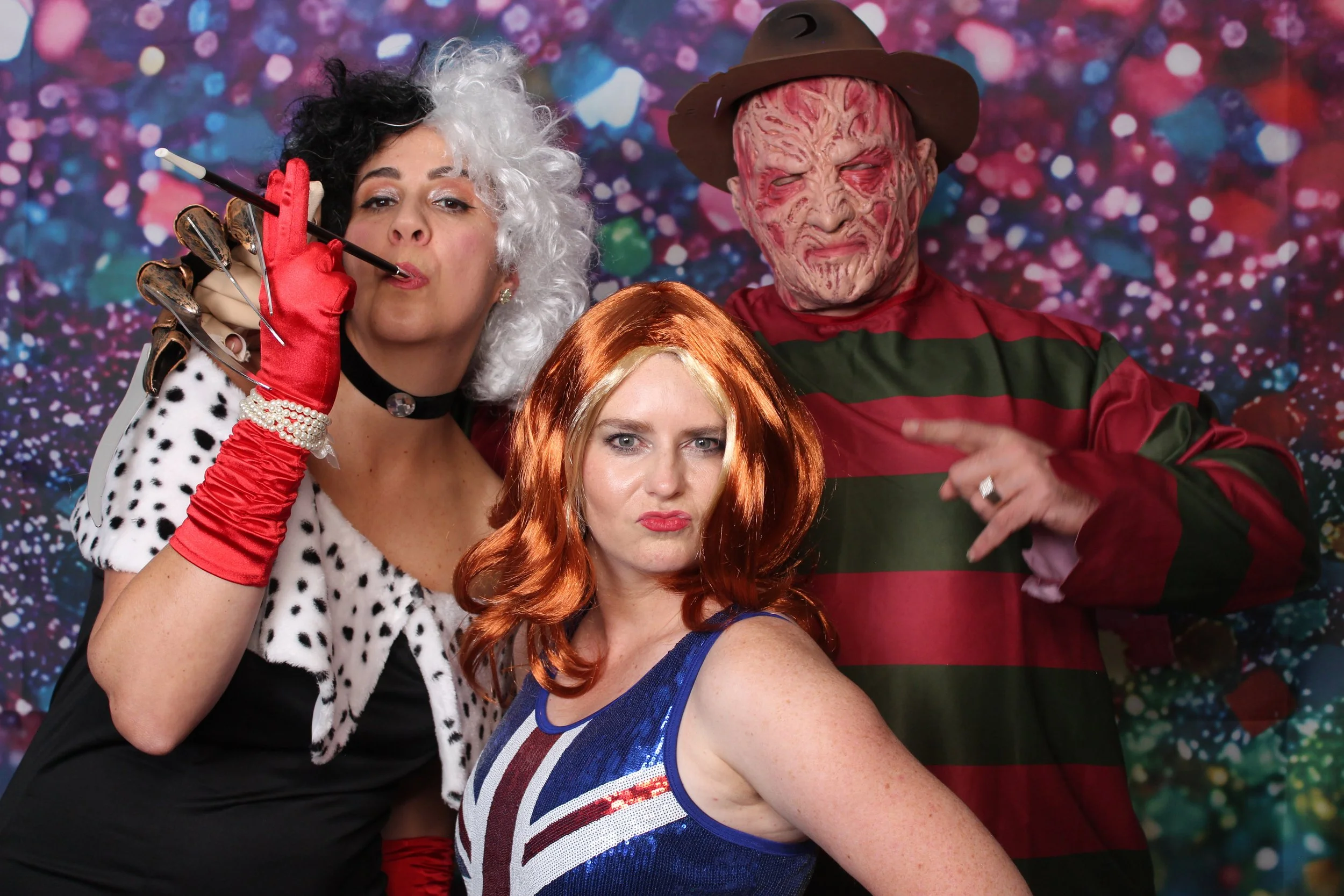 Four people dressed in 90s themed costume posing together in front of a colorful, sparkling background with our open air photobooth