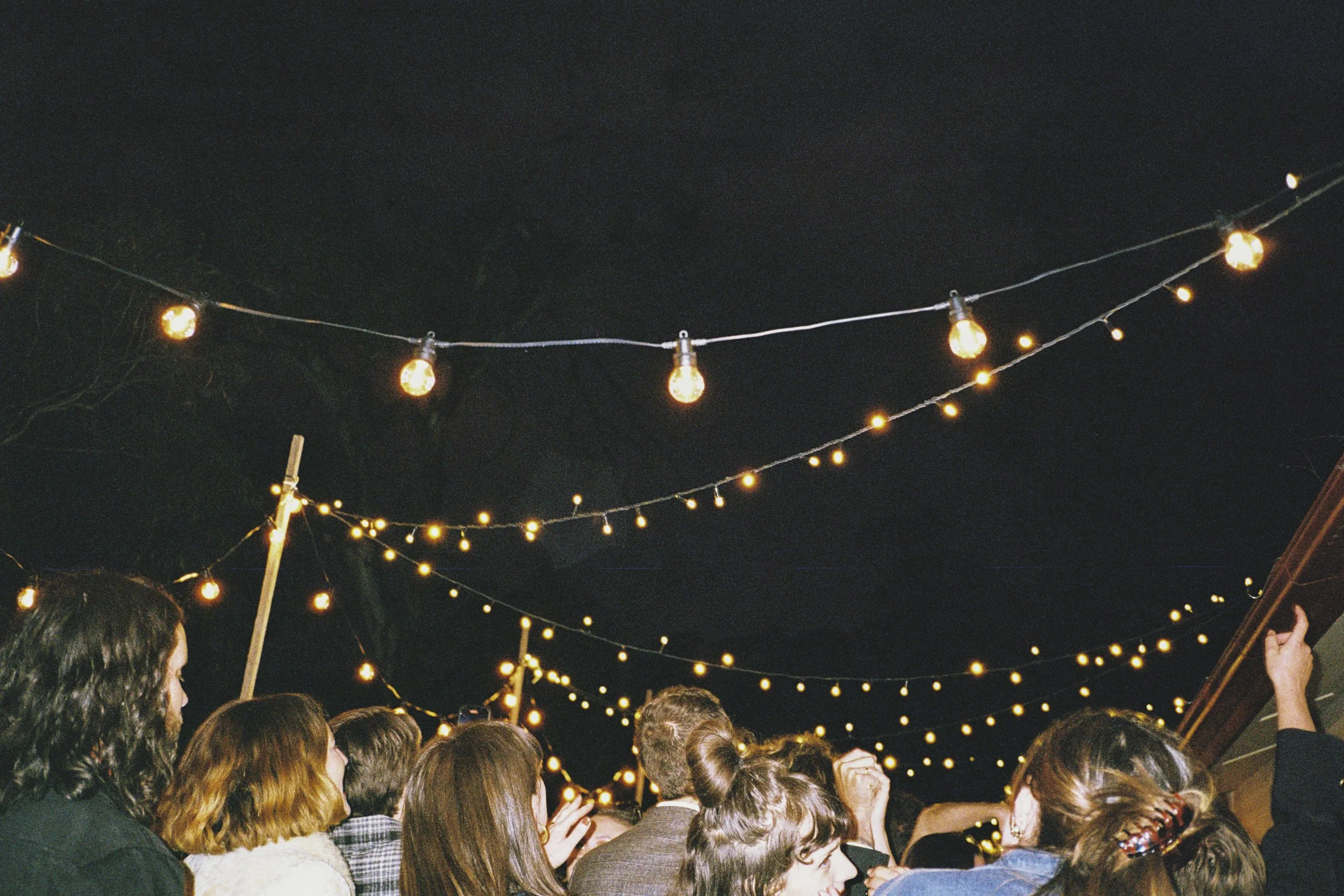 Crowd of people gathered outdoors at night under string lights.