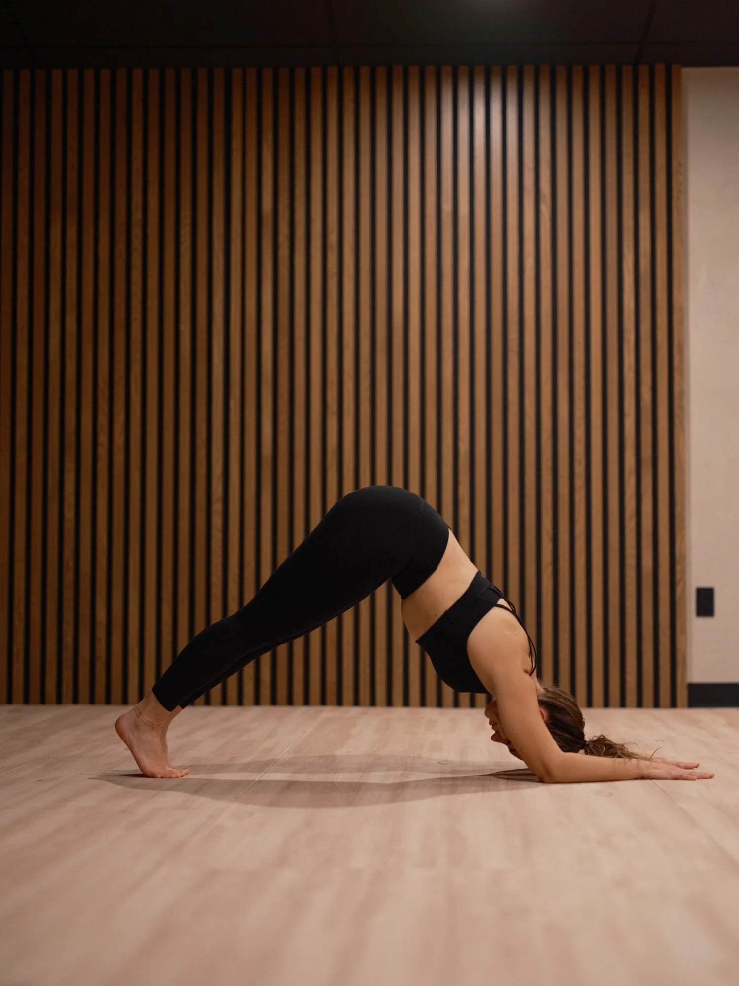 A woman practicing yoga in 8th State Hot Yoga studio, performing a downward dog pose on a light wooden floor.