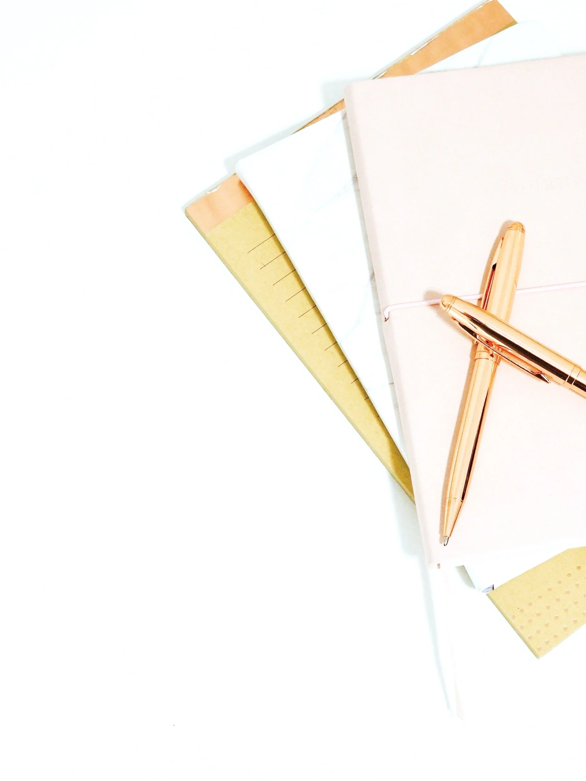 A collection of notebooks of different colors, a gold pen, and a white pencil on a white surface. Karyn Sutton. Strategic marketing and communications professional