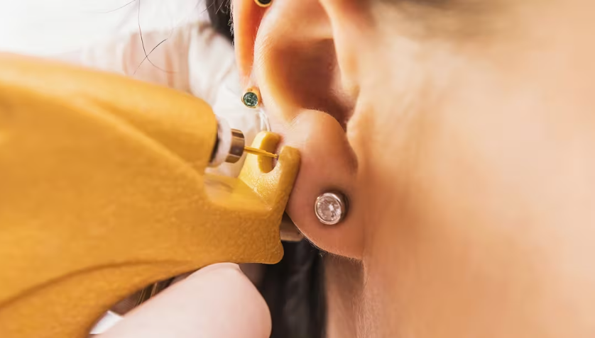 A person receiving a piercing in their earlobe with a piercing gun.