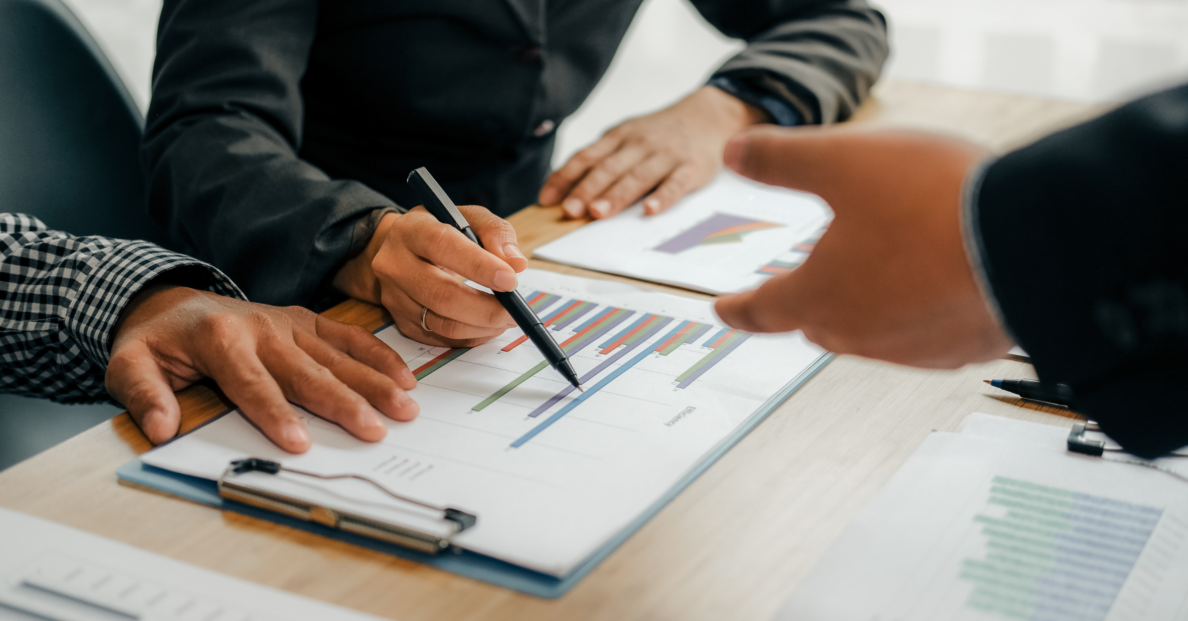People discussing business charts and graphs during a meeting, using pens and documents on a table.