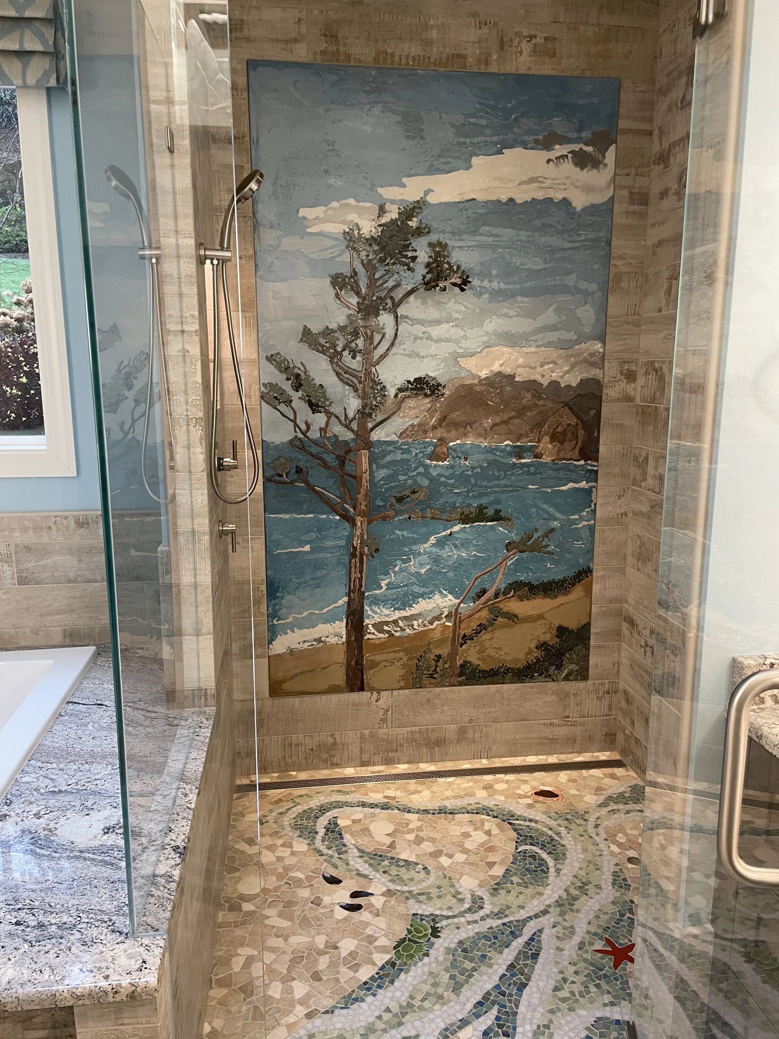 A mural of a coastal landscape with a tree, ocean waves, rocks, and sky, located in a bathroom shower area with mosaic floor tiles and wooden wall panels.