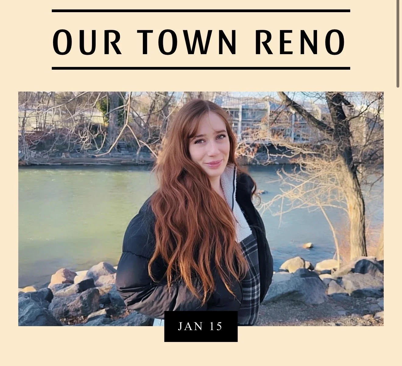 A young woman with long red hair standing near a river, wearing a black jacket and plaid shirt, with trees and buildings in the background.