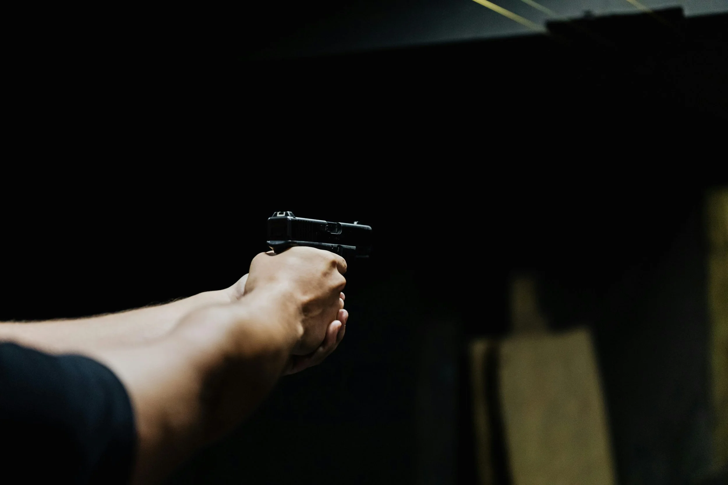 A person holding a black pistol, aiming it forward in a dark environment.