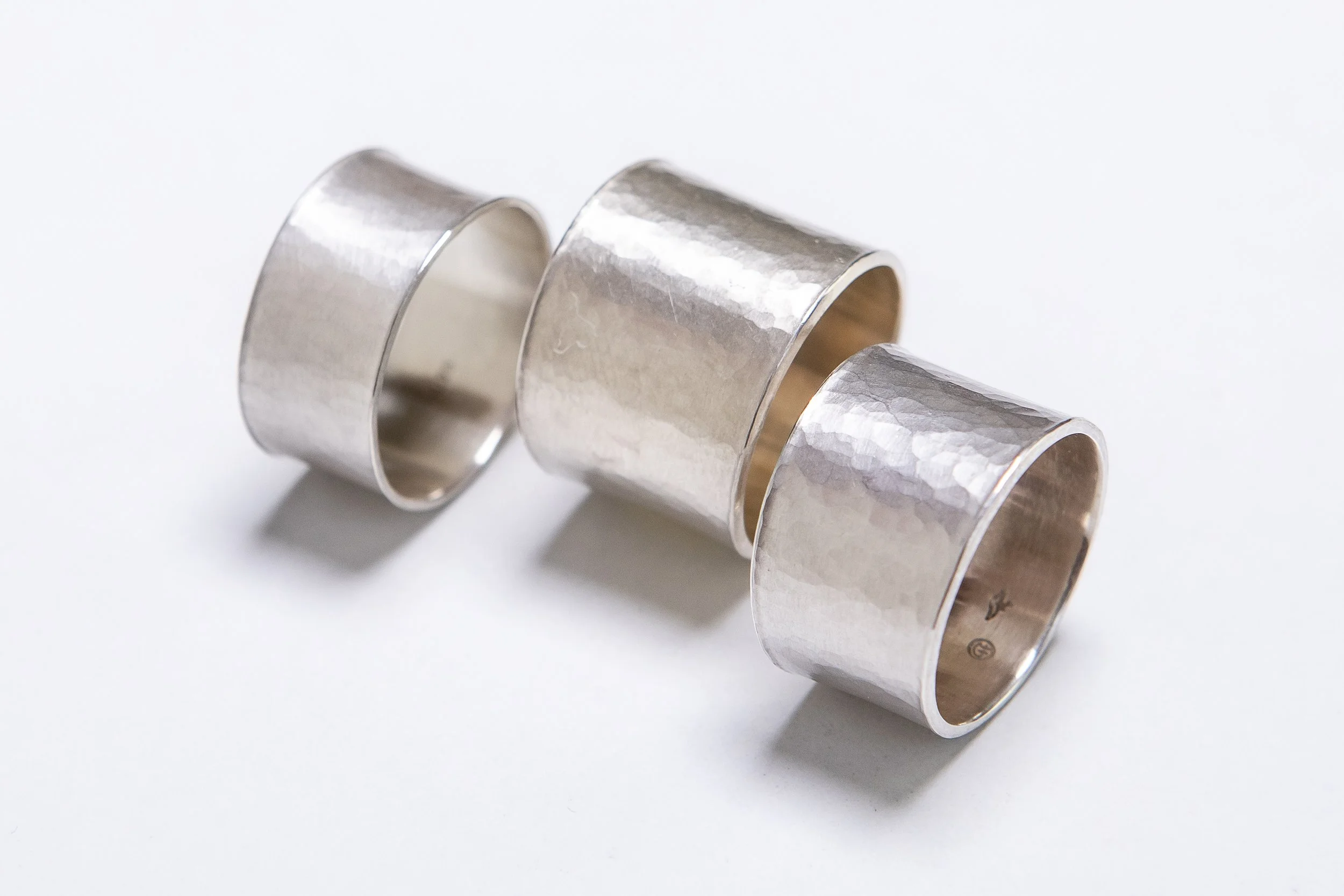 Drei silberne, breite, gewellte Metallringe auf weißem Hintergrund.