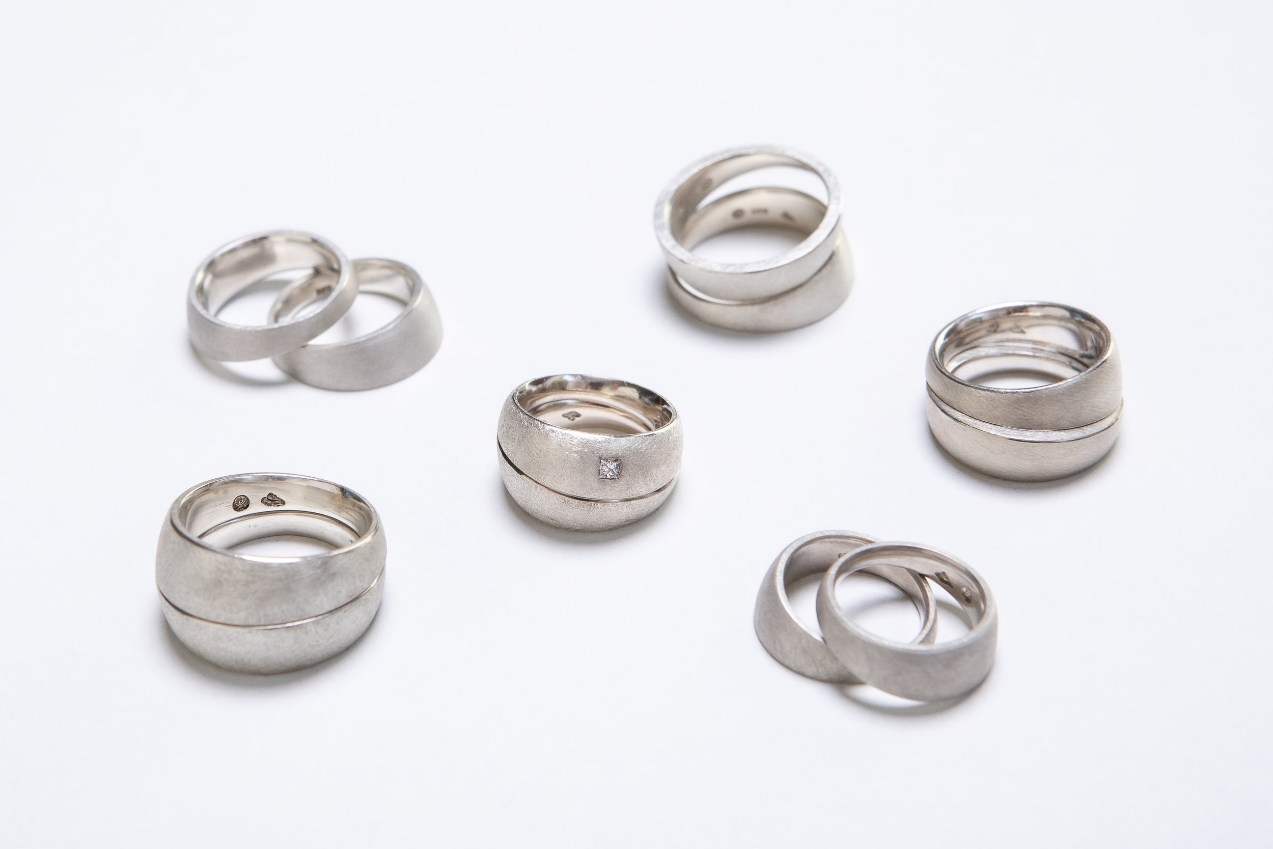 Mehrere silberne Eheringe auf weißem Hintergrund, einige mit kleinen Diamanten.
