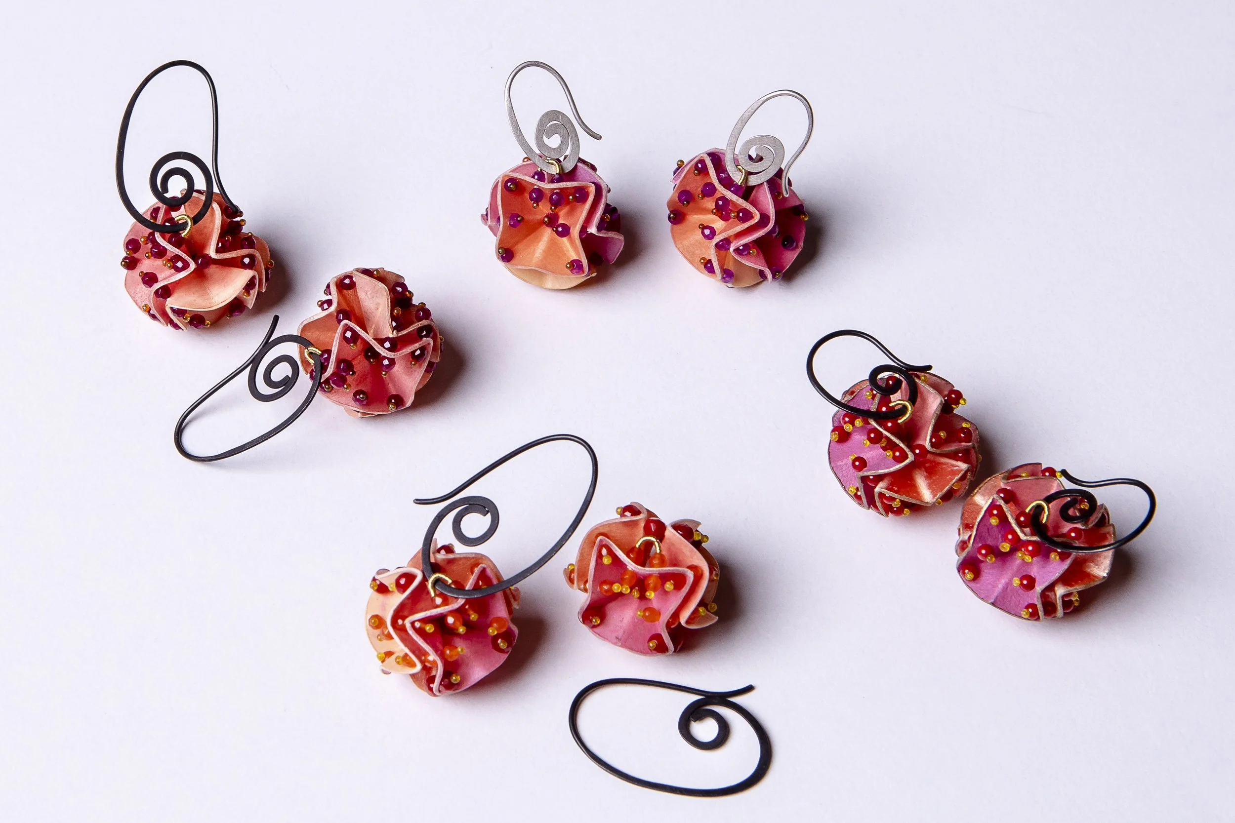 Fünf Paar handgefertigter Ohrringe in rosa und orange mit roten und gelben Perlen, auf weißem Hintergrund.