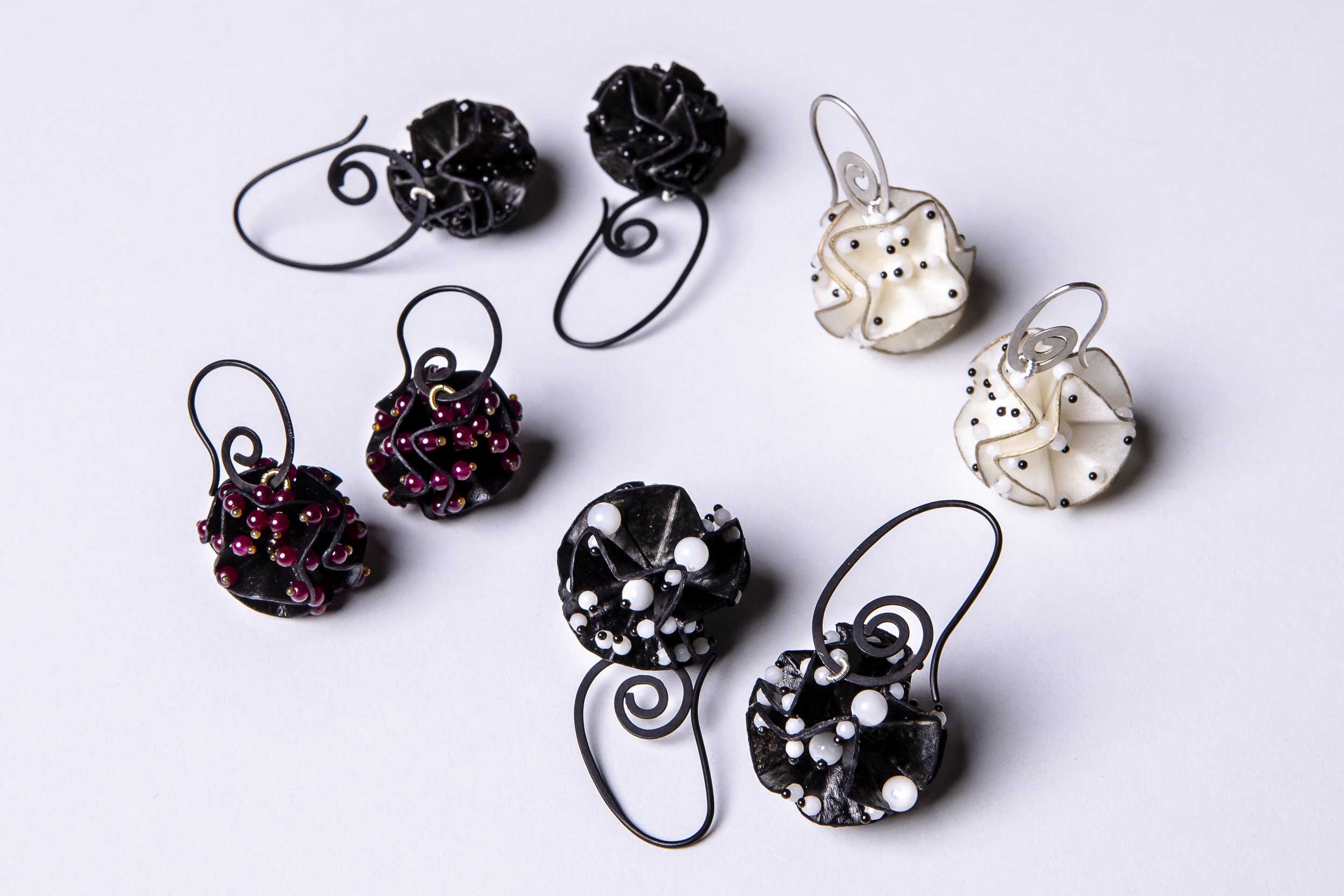 Kunstvoll gestaltete Ohrringe mit Perlen in Schwarz, Weiß und Rot, auf weißem Hintergrund.