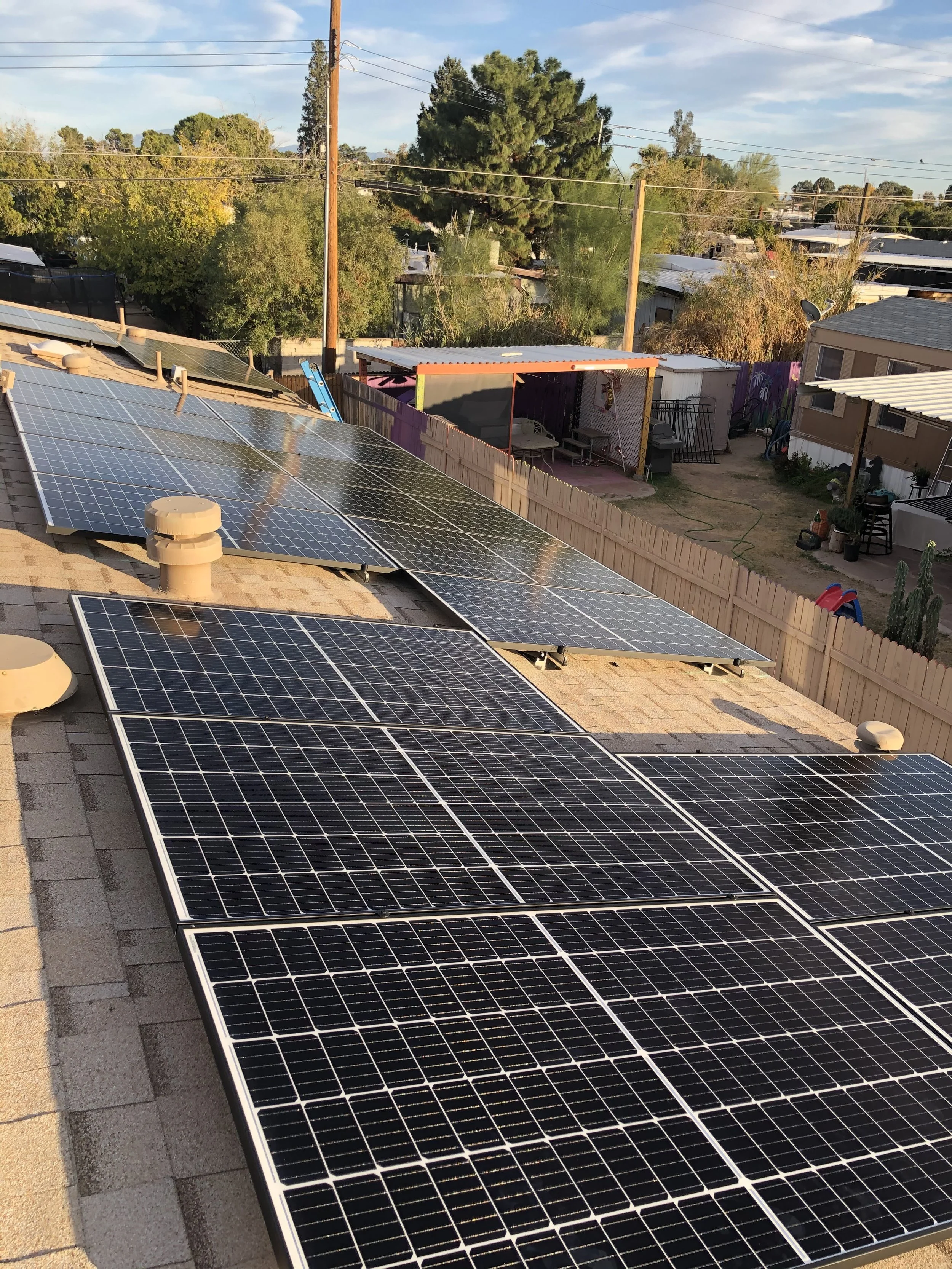 Multiple solar panels installed on a residential roof in a neighborhood with trees and houses in the background.