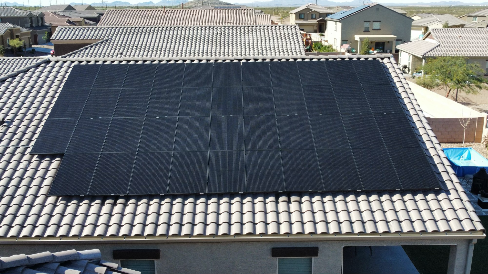 Rooftop with black solar panels installed on a tiled roof in a suburban neighborhood.