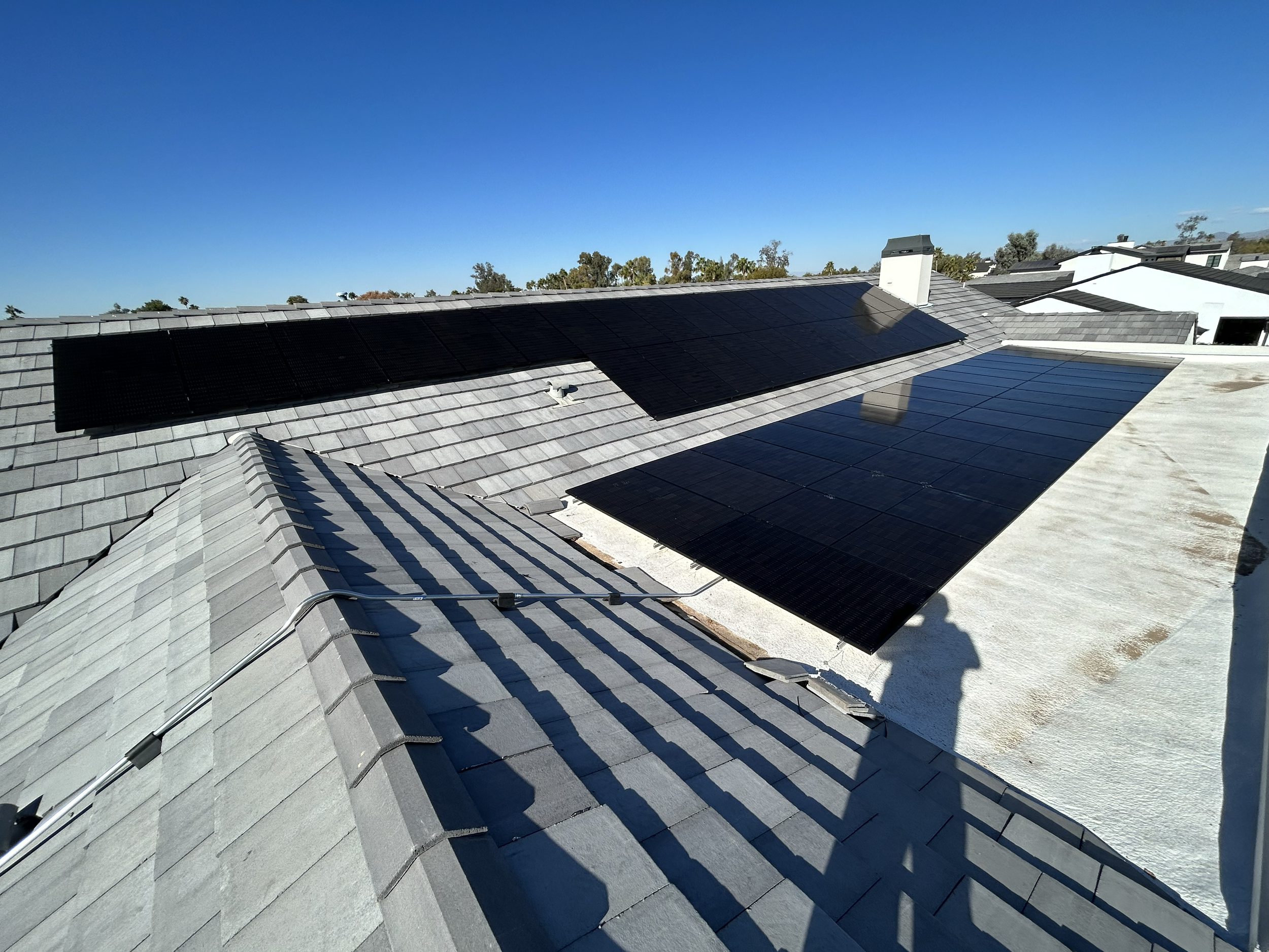 Roof with black solar panels installed on gray shingles under a clear blue sky.