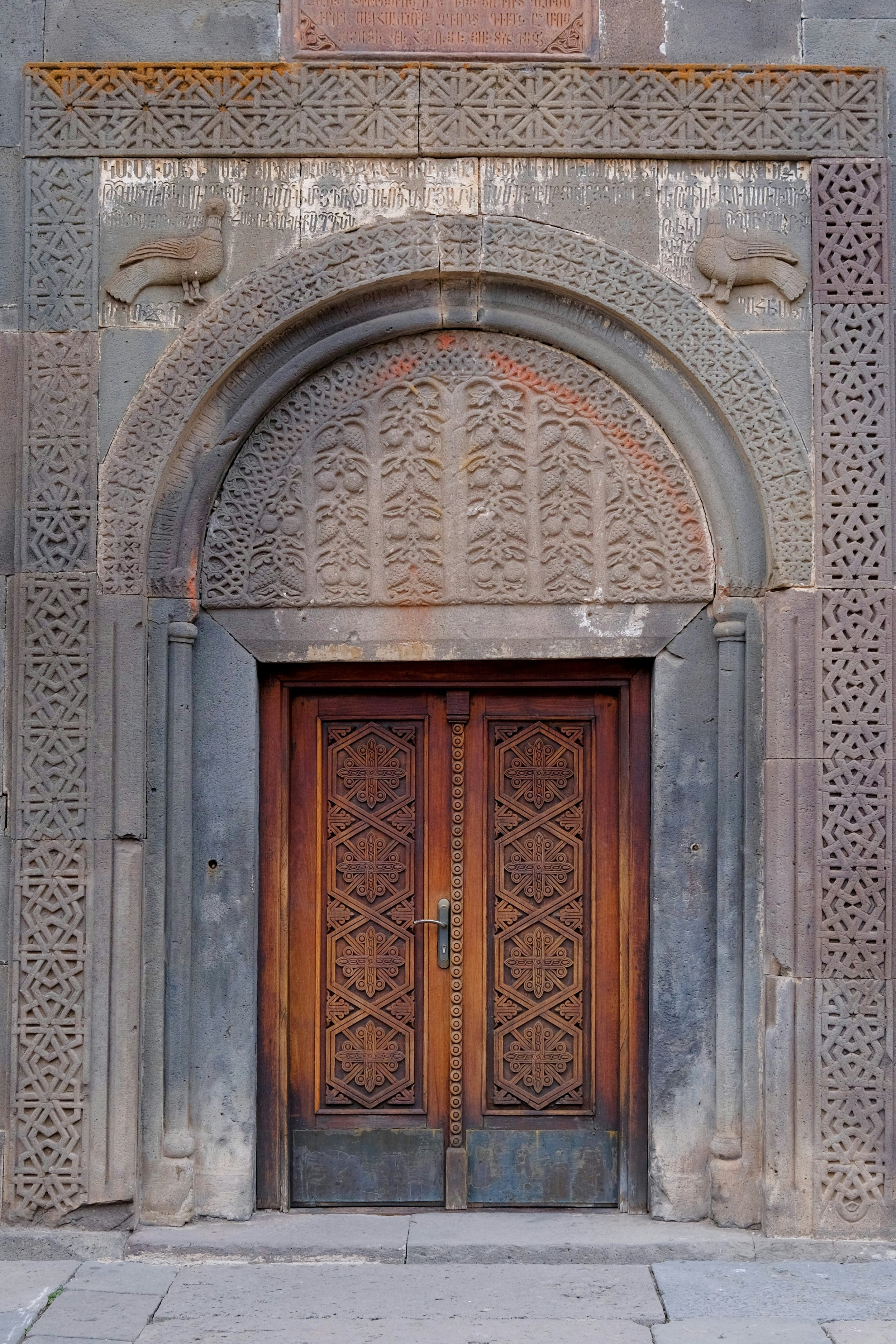 Ornate wooden doors surrounded by intricate stone carvings in Geghard, Armenia. Photograph by Kseniia Zapiatkina.