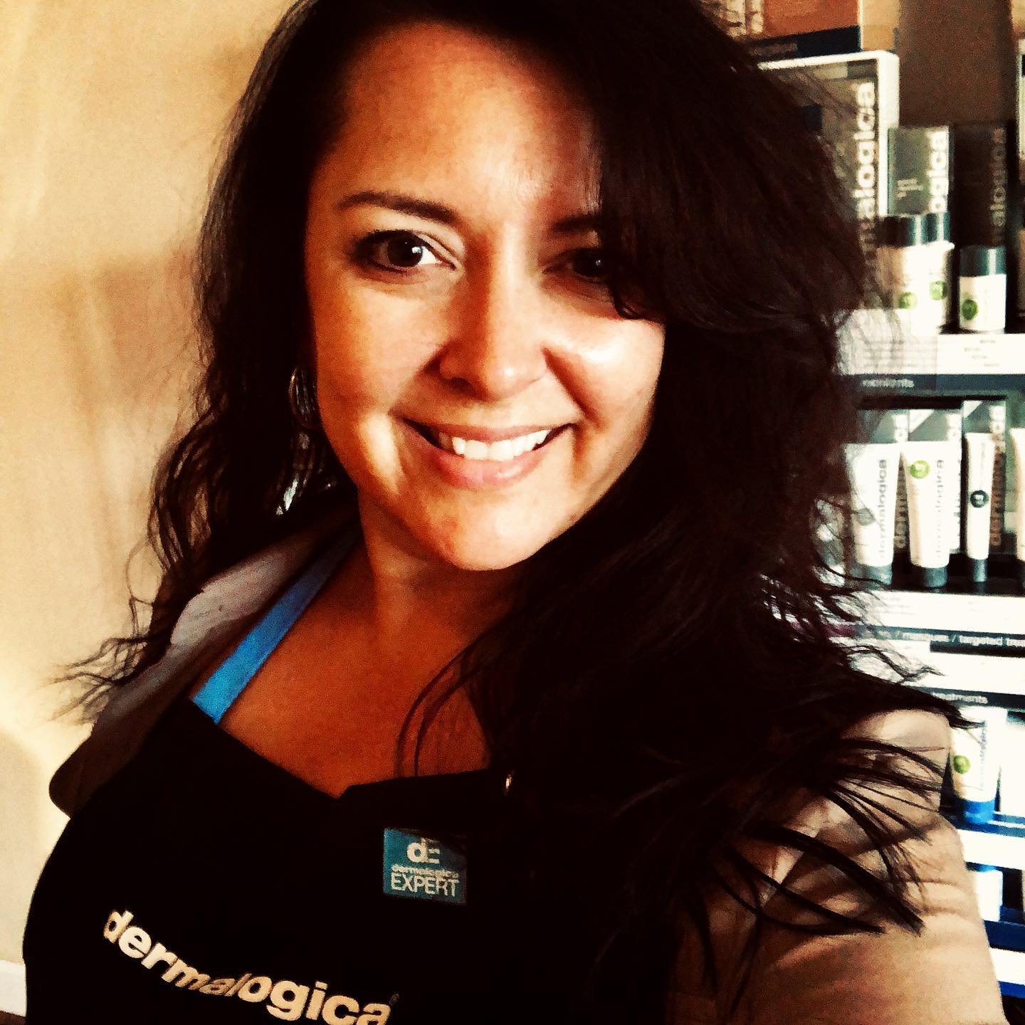 Smiling woman with long dark hair taking a selfie in front of a bookshelf.