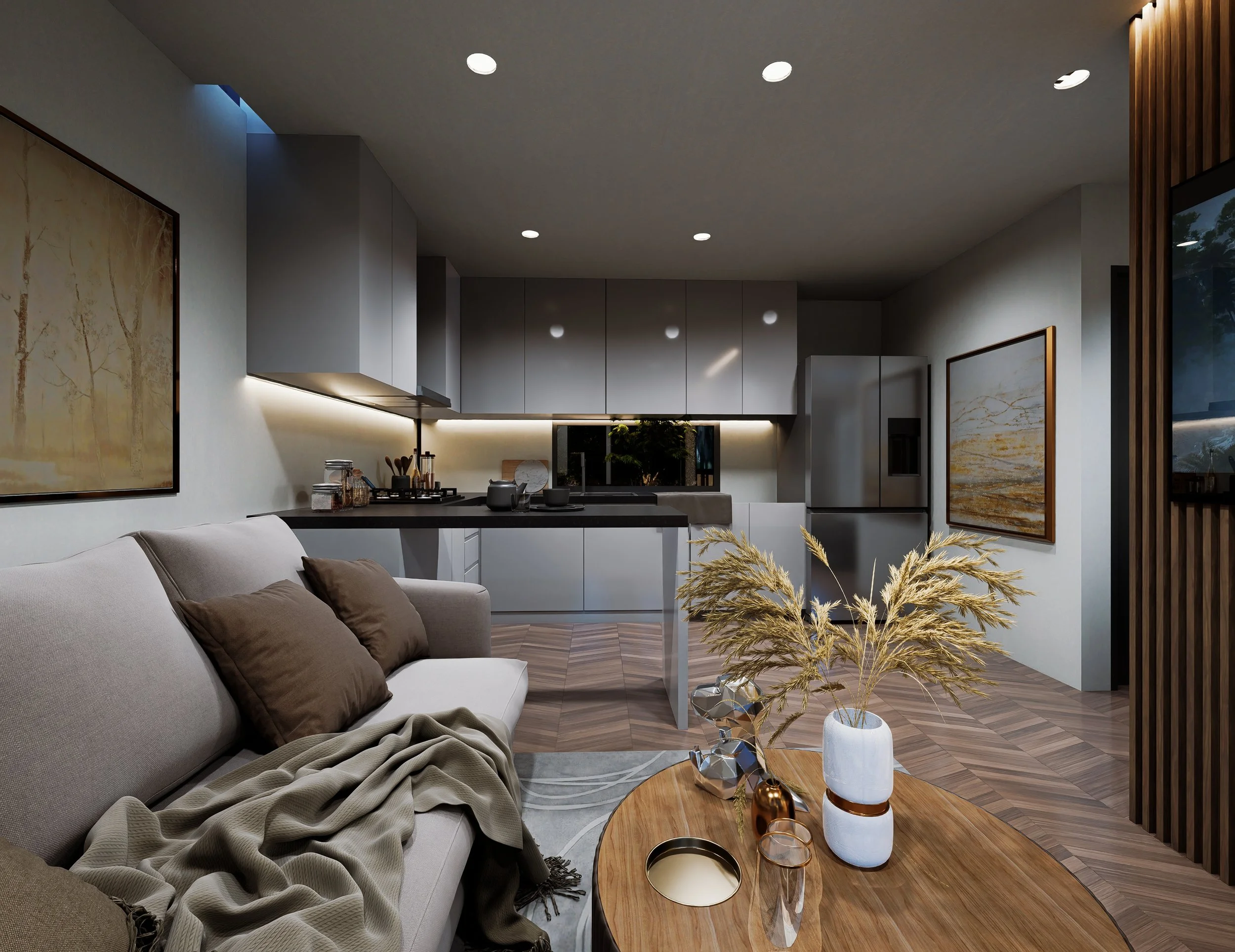 Modern living room with a beige sofa, brown pillows, and a throw blanket, facing a wooden coffee table with decorative vases and a large vase with dried plants, open kitchen with gray cabinets and a window behind, wooden flooring, and wall art.