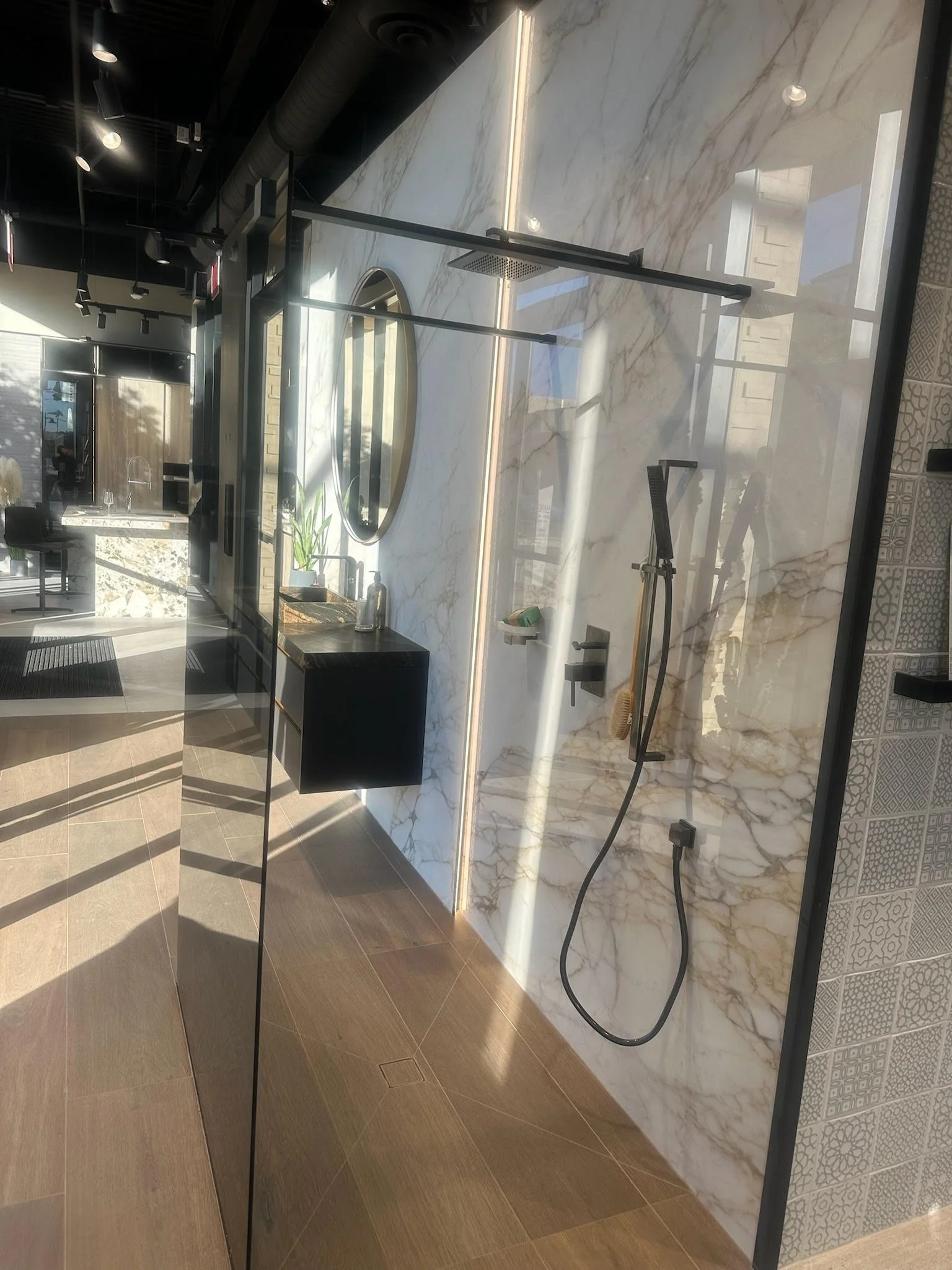 Modern bathroom shower with marble wall, black fixtures, and a glass partition.